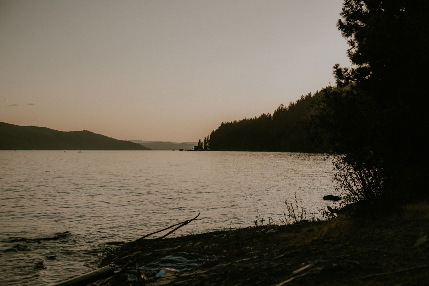 Panoramic view of a serene lake at sunset with silhouetted trees and mountains in the background.