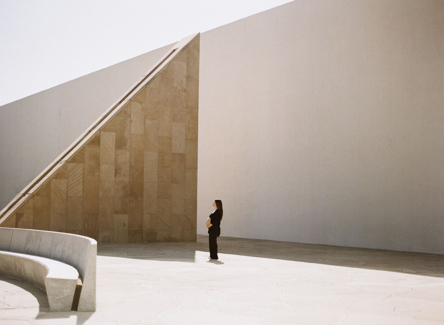 Moving figure creates an engaging visual journey across minimalist architectural spaces with angular walls and dramatic shadows.