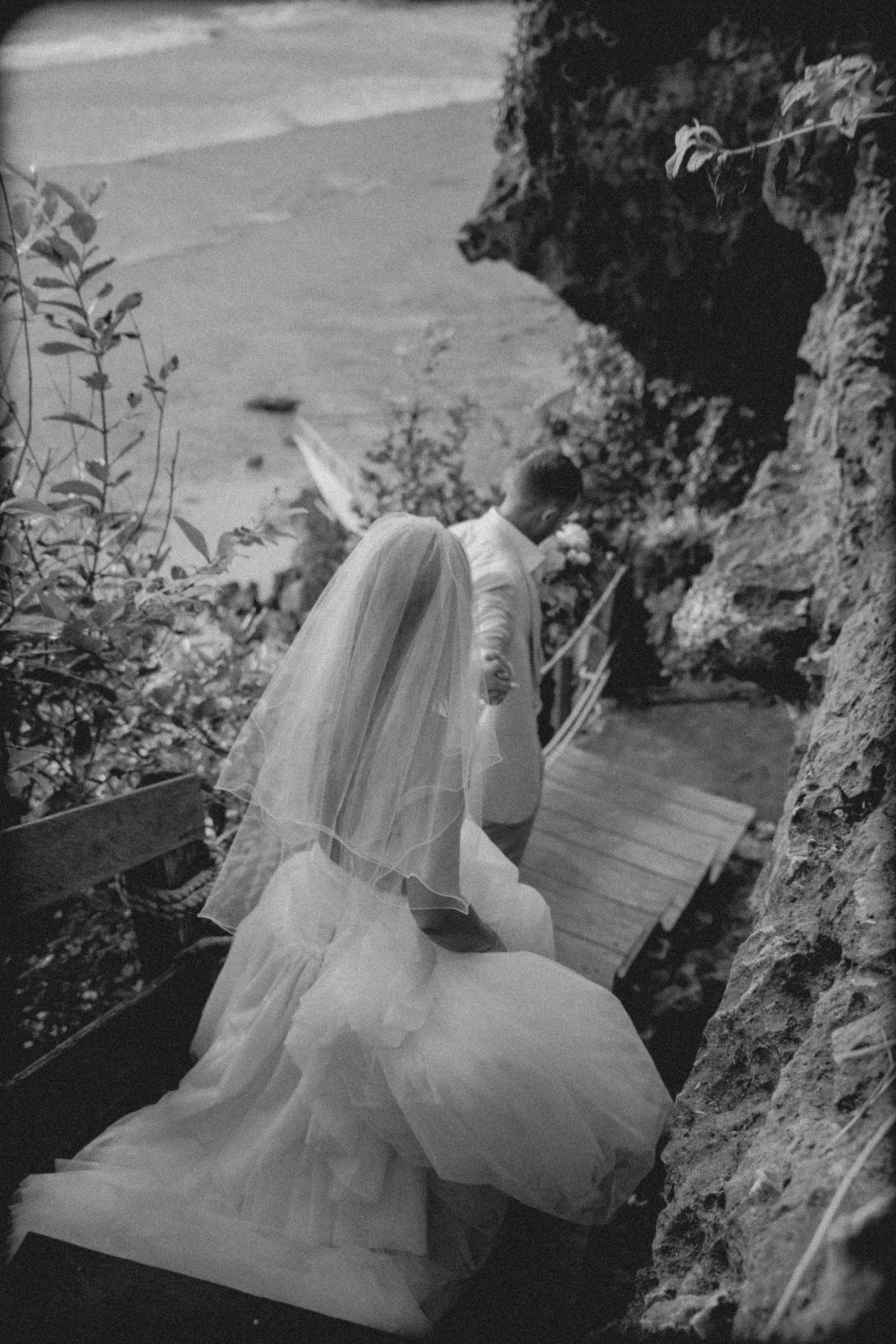 Silhouetted couple sharing a romantic kiss under flowing wedding veil at sunset with dramatic sky in background.