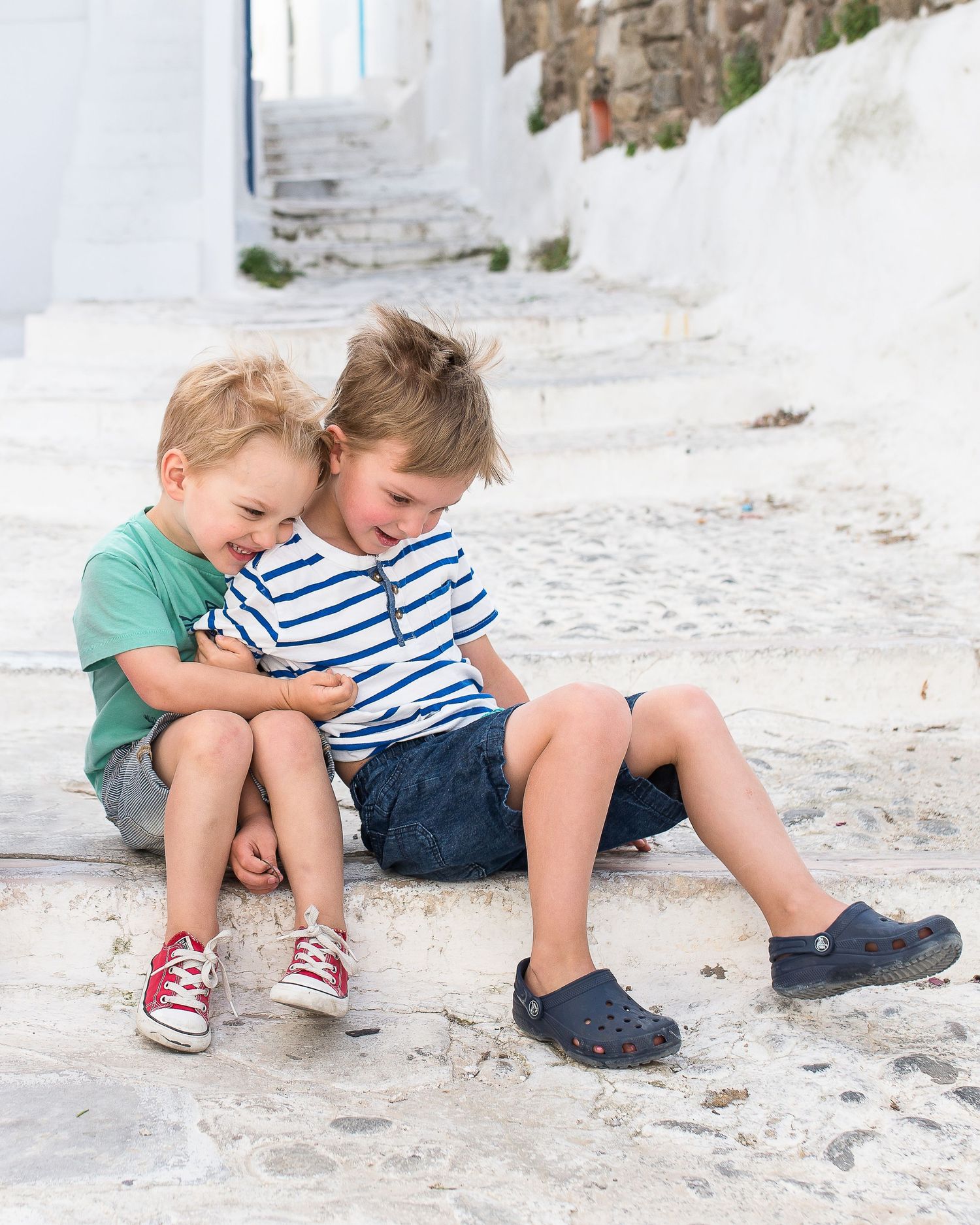 Two children sitting together on white stone steps Greek village in casual summer clothing.