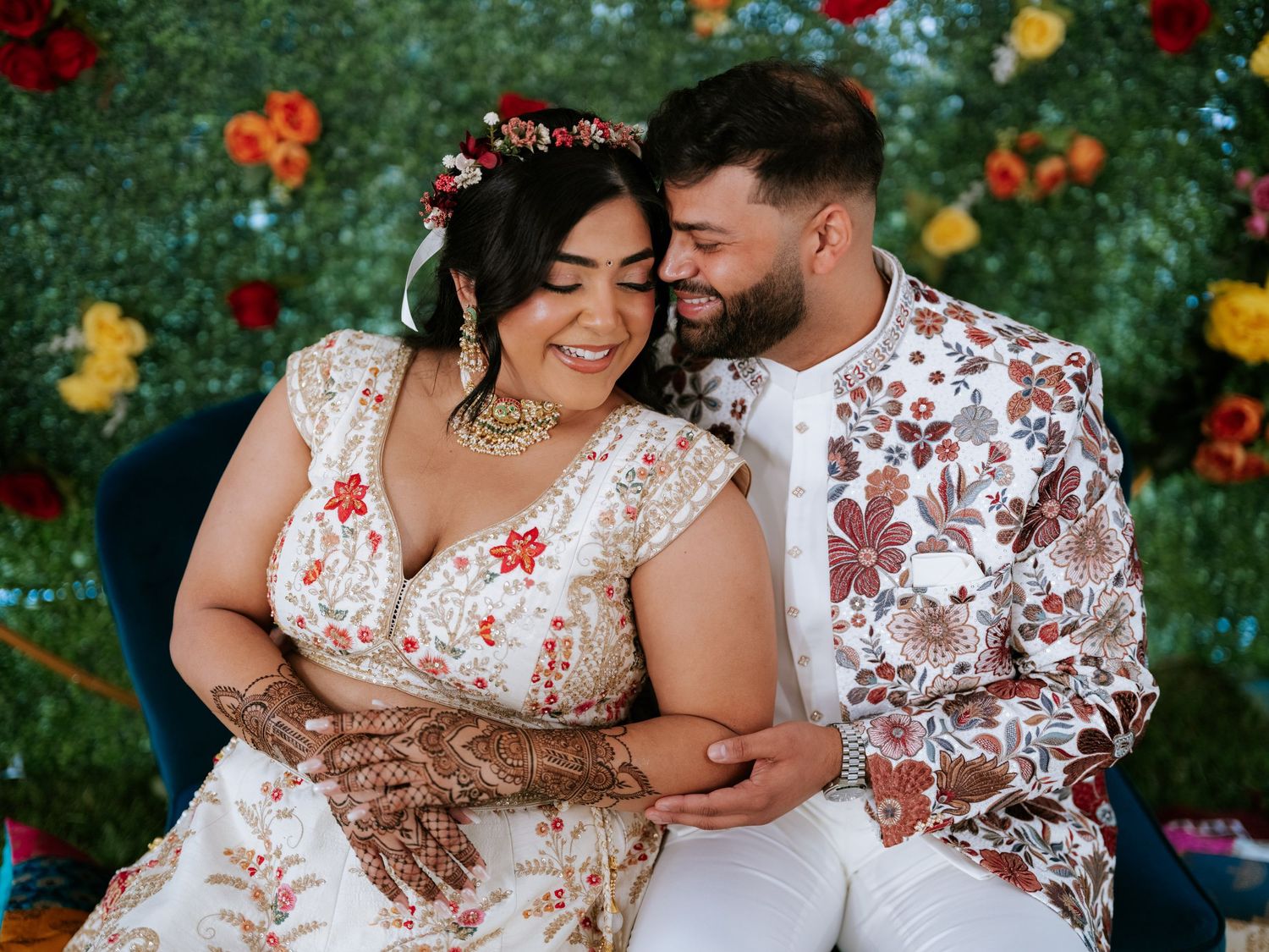 A romantic couple in coordinating floral outfits embrace in a vibrant garden with red and orange blooms.