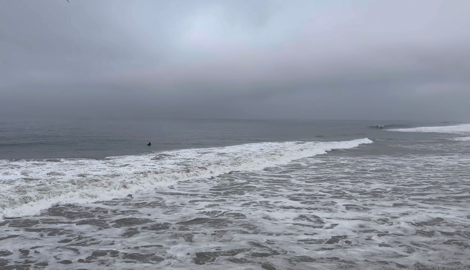 Stormy gray ocean waves crash under an overcast sky along a moody coastline.