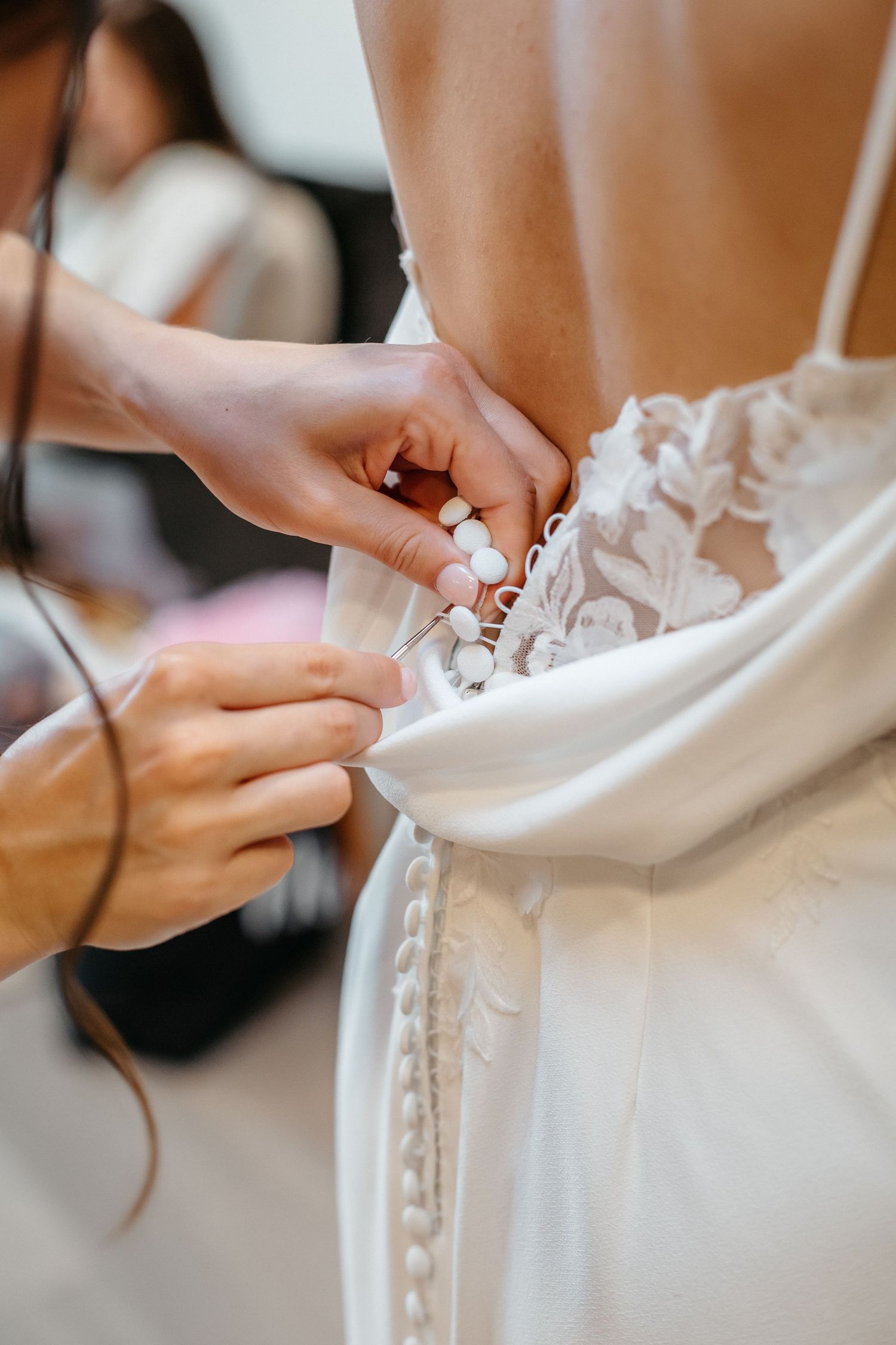 Close-up shots of hands adjusting and fastening buttons on the back of an elegant white wedding dress.