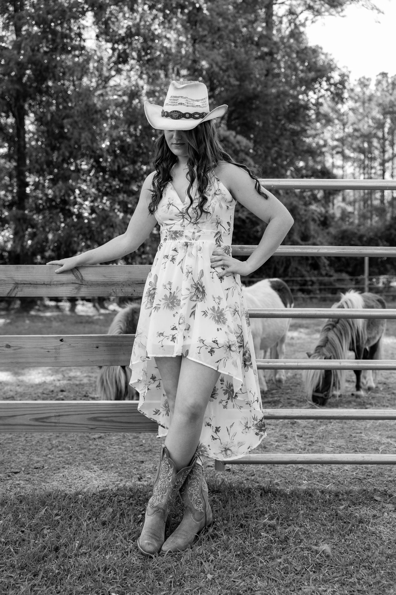 Black and white photo series showing boots and a floral dress in a rustic outdoor setting with wooden fencing.