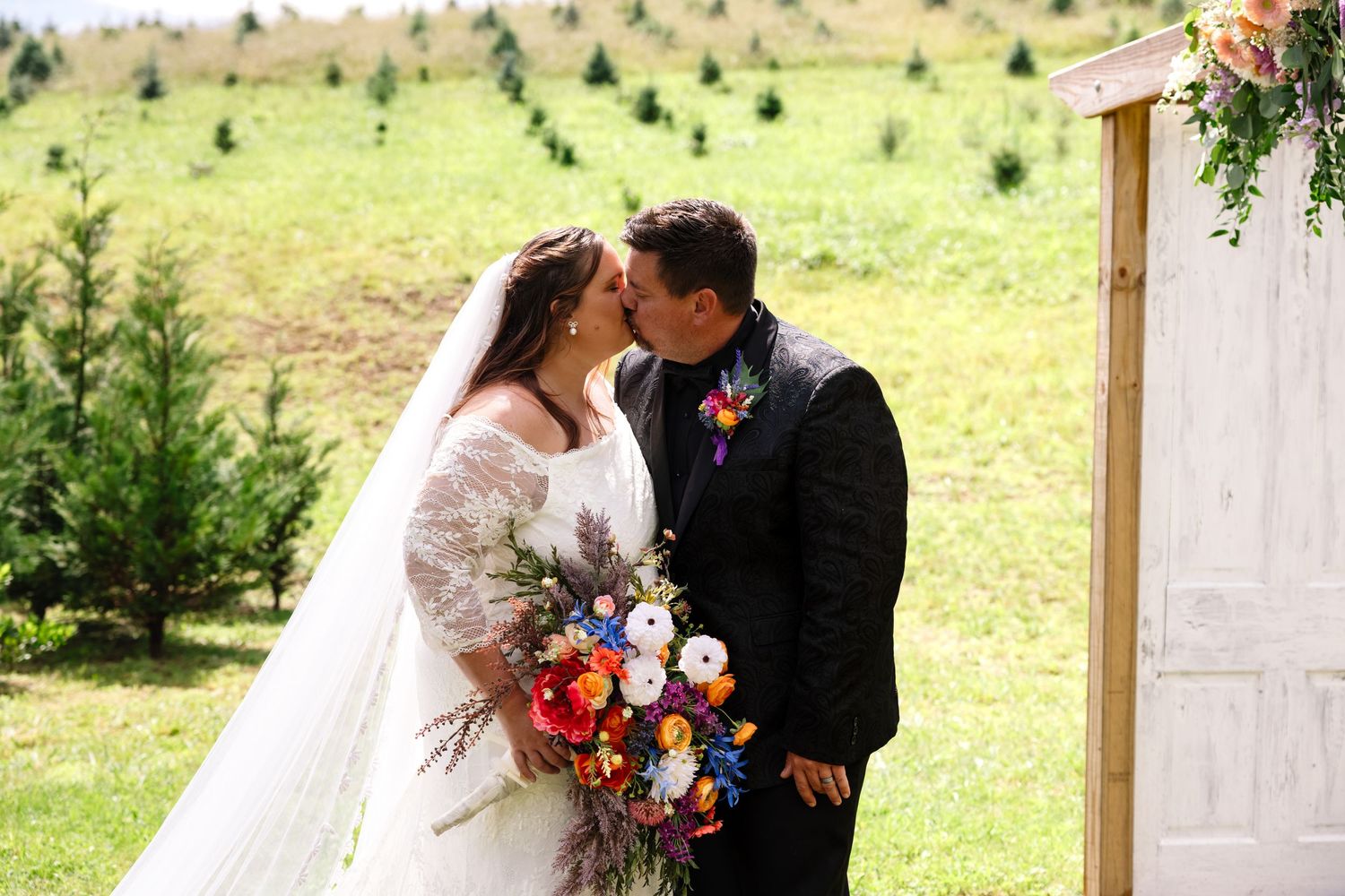 A couple shares a romantic embrace during their autumn wedding ceremony with colorful fall foliage in the background.