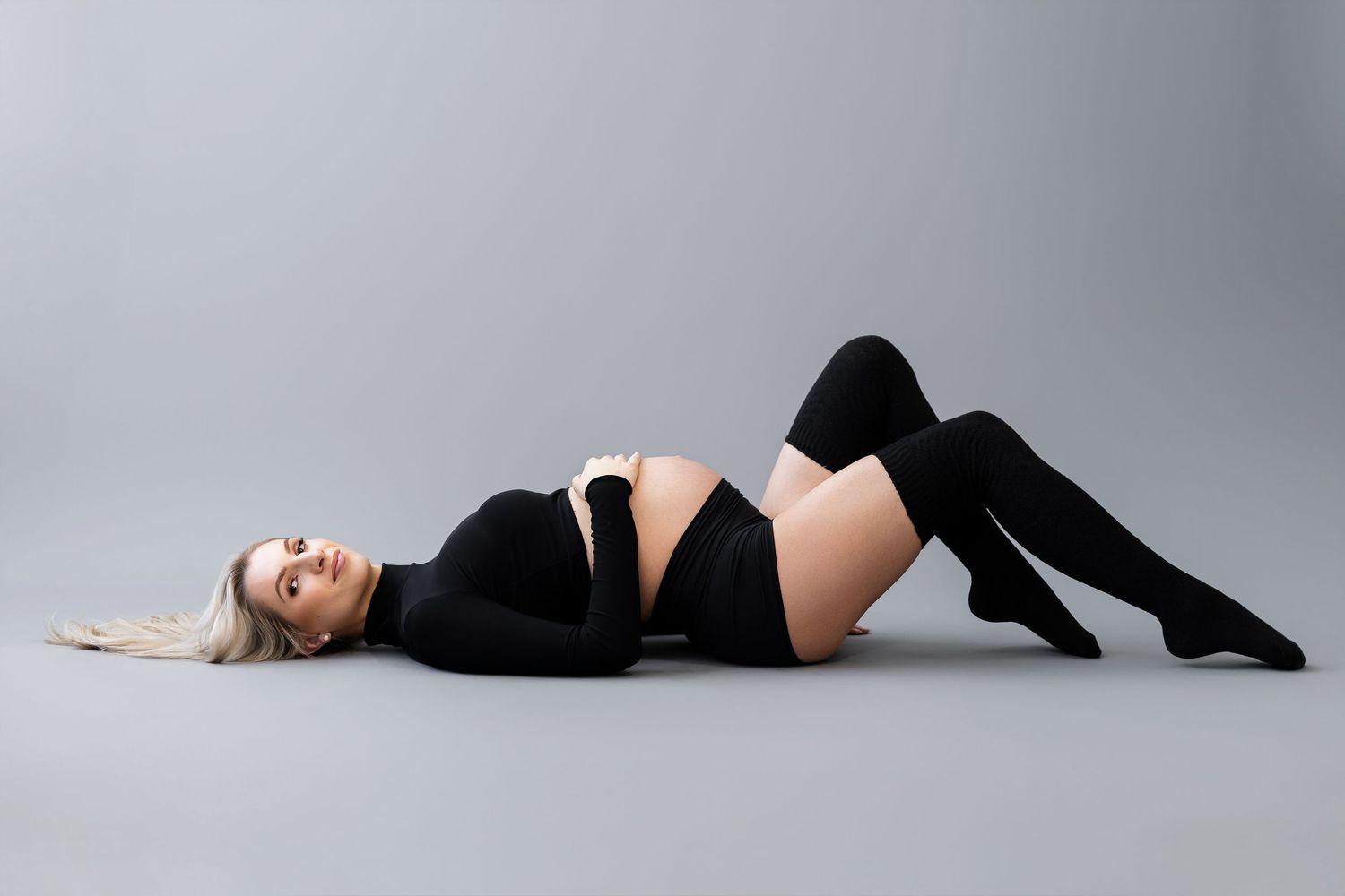Maternity photo with woman in black outfit lying on grey background.