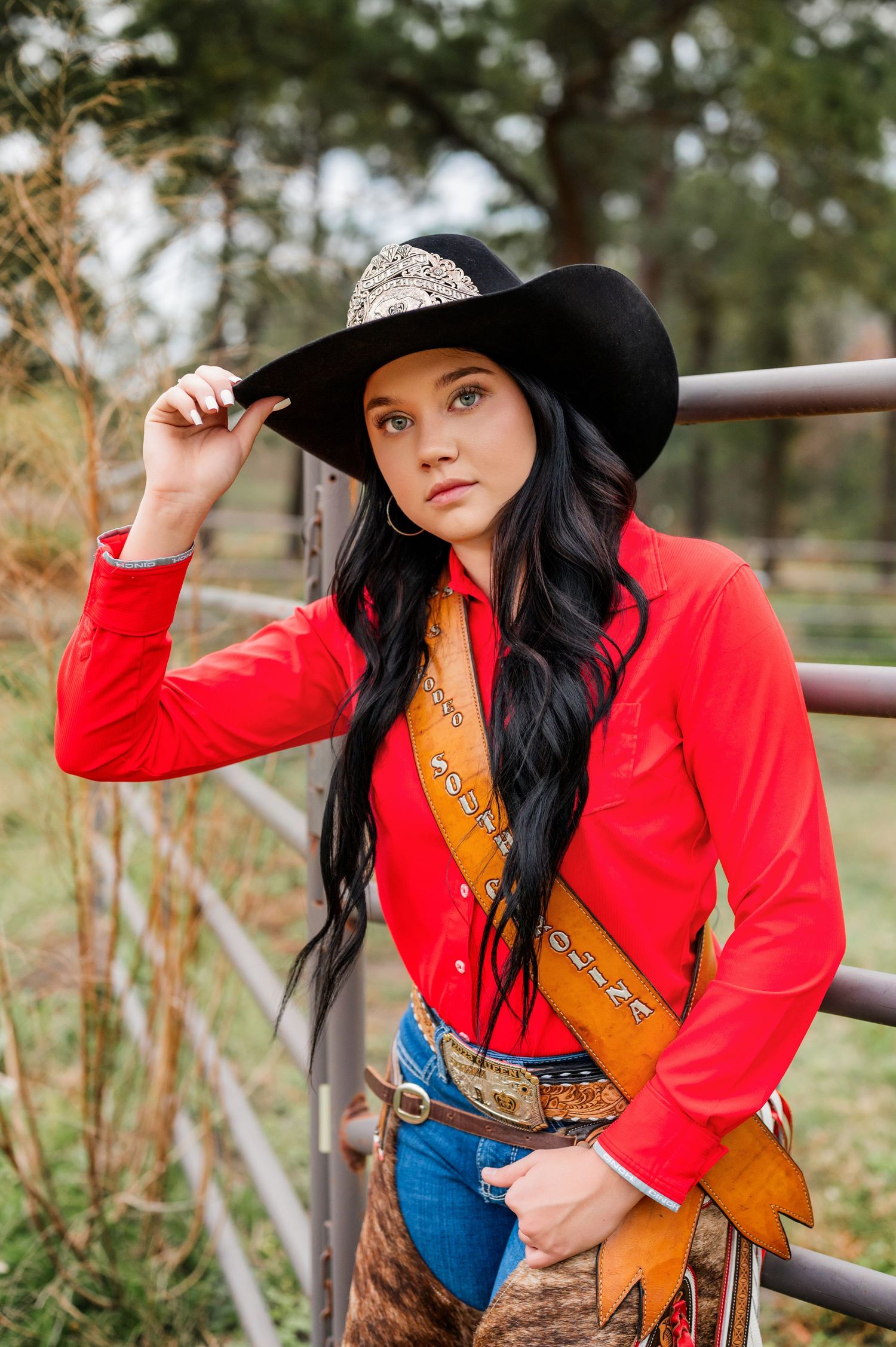 Western style photoshoot with red jacket, black hat, and rustic fence background.