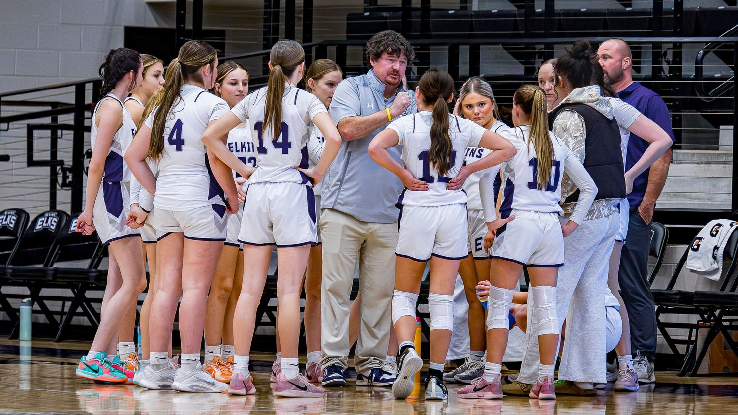 Basketball teams line up in a circle on the court during a pre-game ceremony or moment of silence.