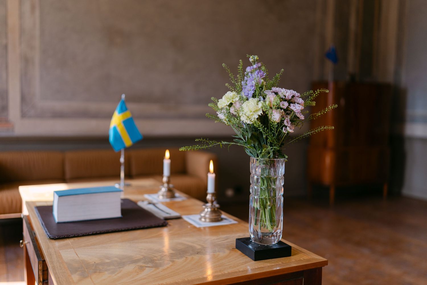 Elegant wooden table with Swedish flag, lit candles, books, and a crystal vase of fresh flowers in a classic interior.