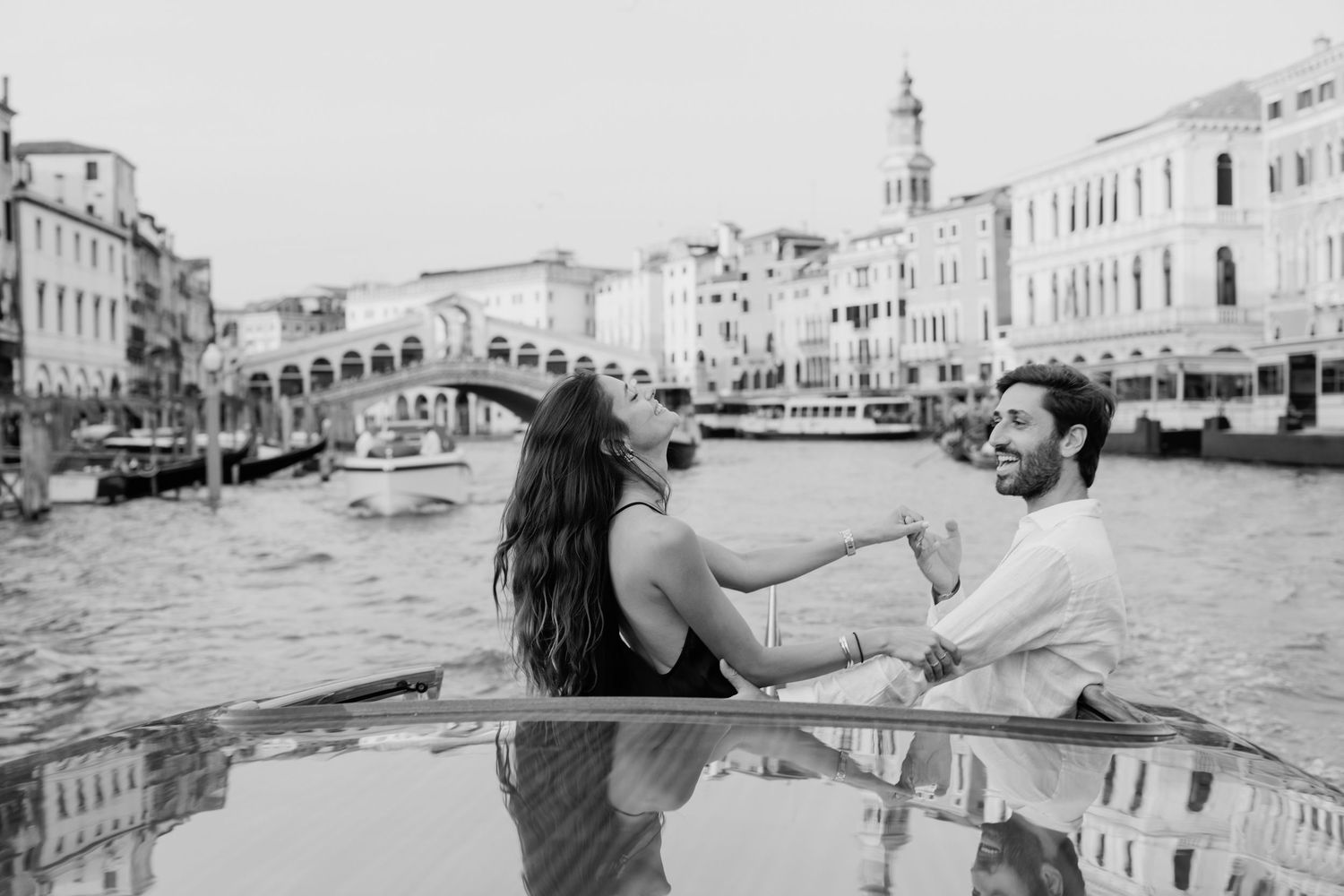 Couple holding hands on a rooftop terrace at sunset with Venice cityscape in the background.