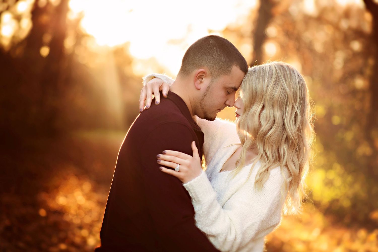Romantic couple sharing a tender moment in golden autumn sunlight, surrounded by warm fall foliage.