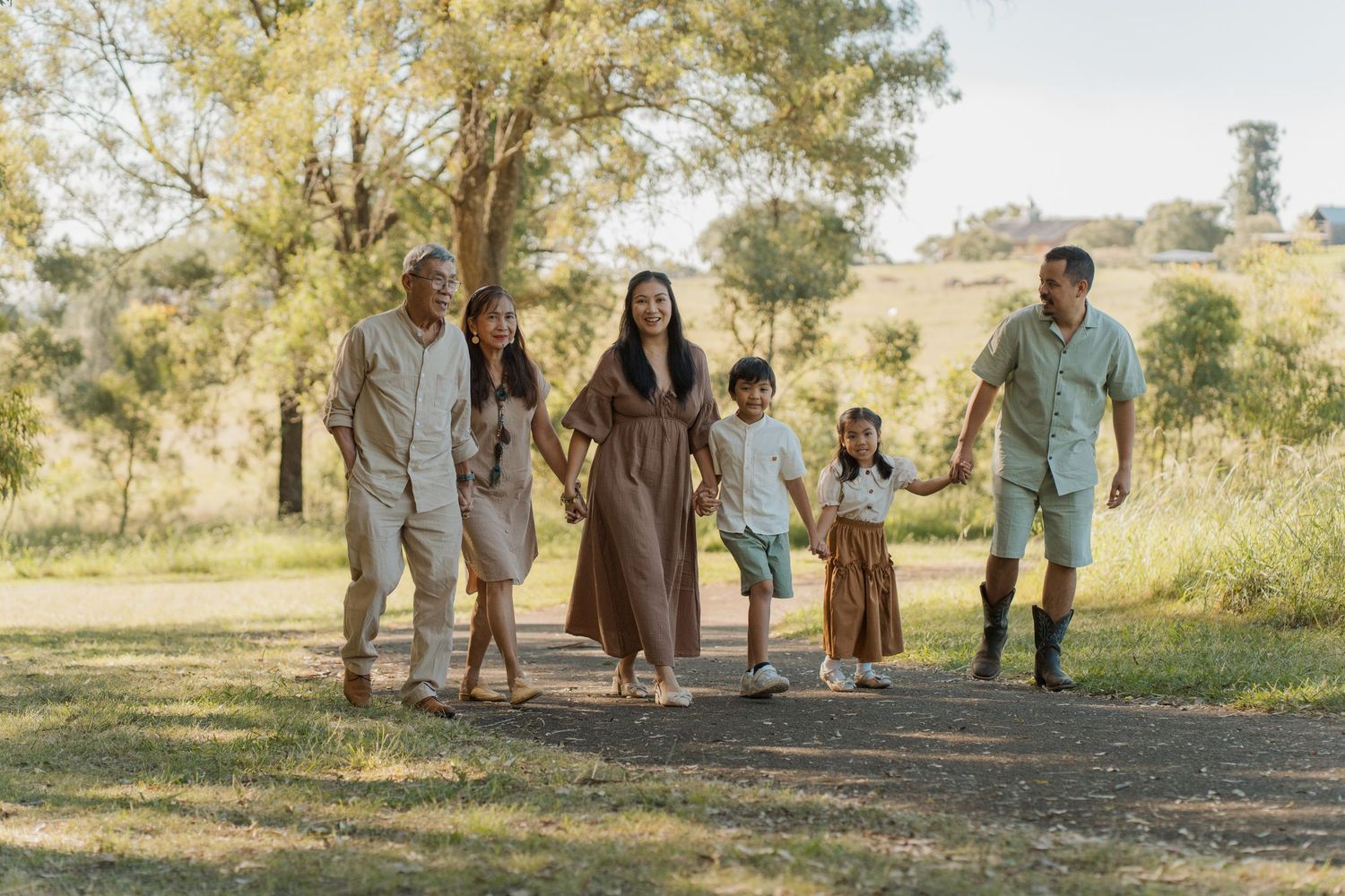 A happy multigenerational family walks hand-in-hand along a scenic park path surrounded by green trees in rouse hill family photoshoot