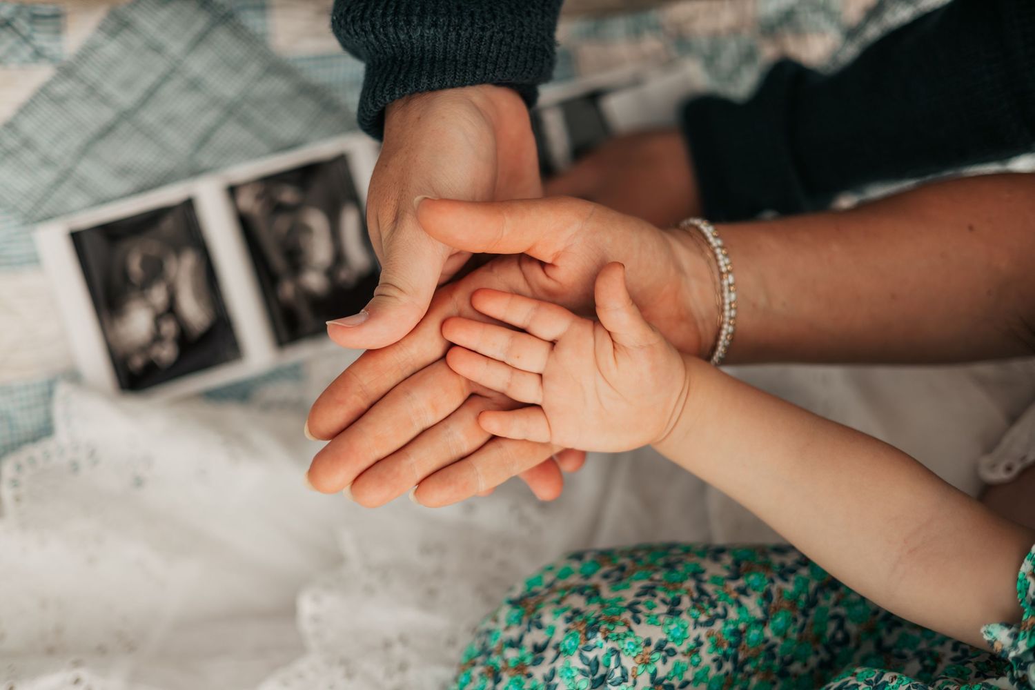 Three generations of hands stacked together near ultrasound photos, symbolizing family love  | Boulder Family Photographer