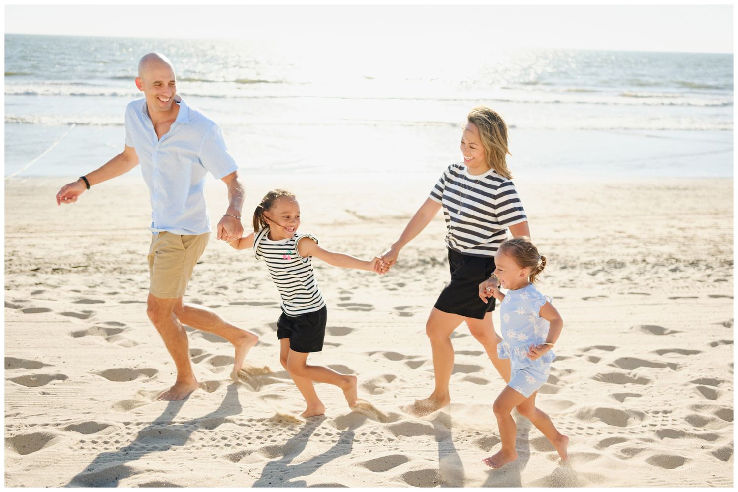 A family plays together on a beach, lifting a child in the air while wearing white clothing in black and white photography.