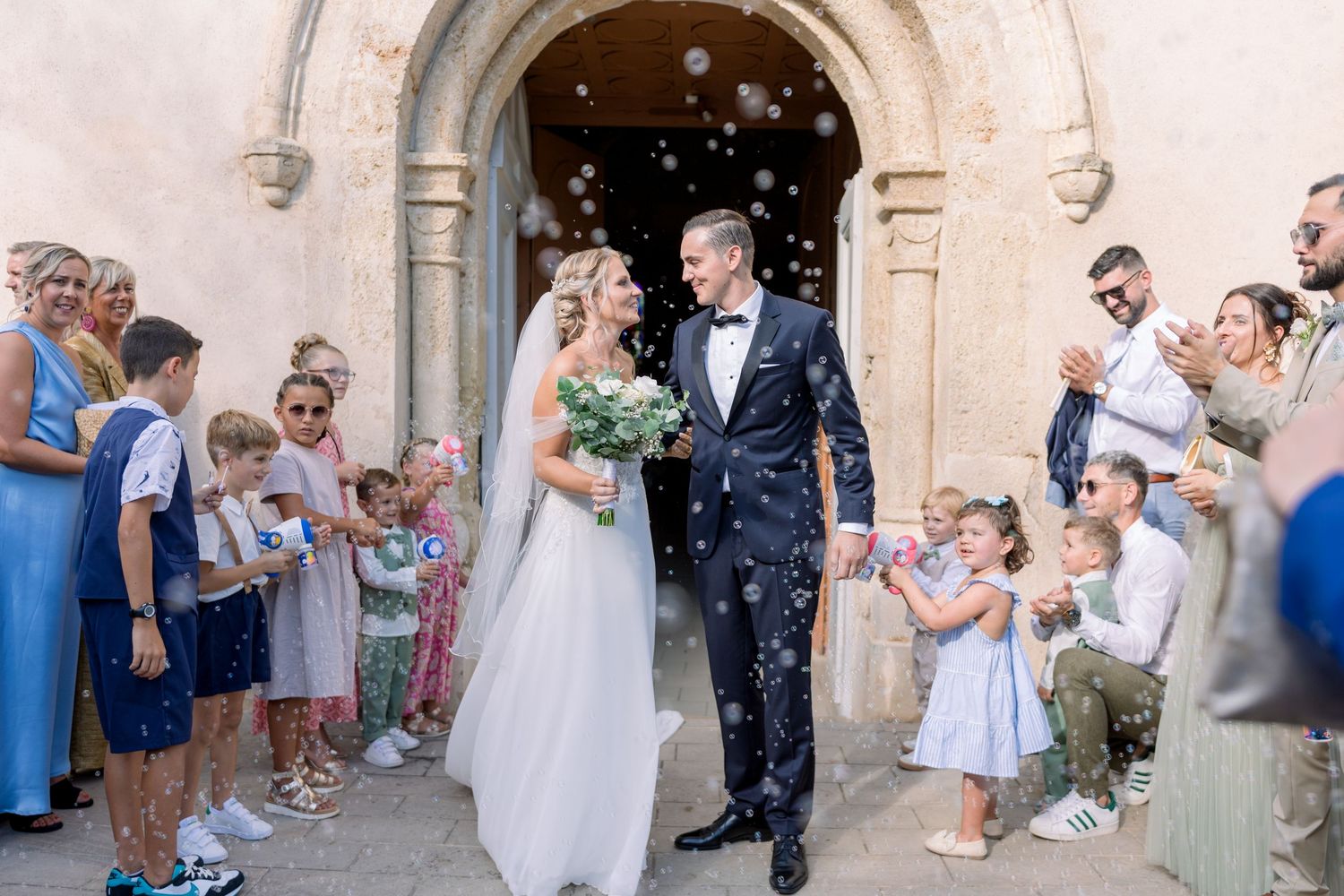 Wedding guests shower newlyweds with confetti as they exit a historic stone church building.