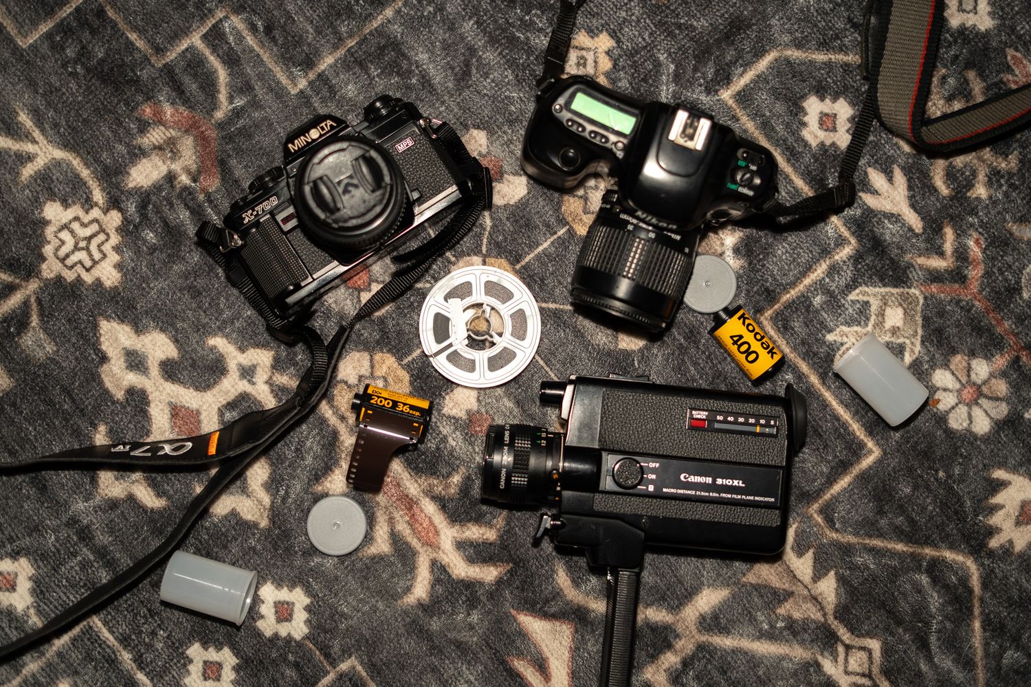 Vintage photography equipment including film cameras, a camcorder, film reels, and rolls on a patterned rug.