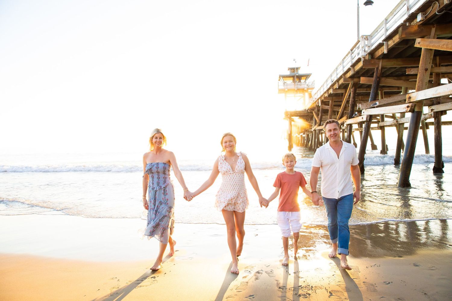A group walks hand in hand along a sunny beach near a wooden pier during golden hour.