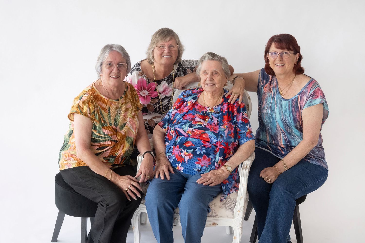 A group of people in casual attire sitting together on white furniture against a light background.
