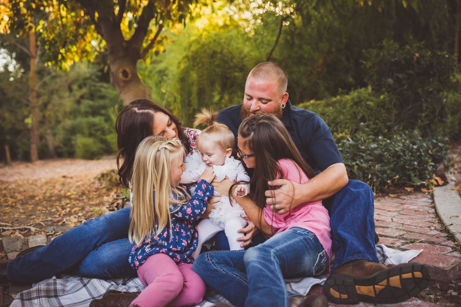 Family of five sharing a warm embrace outdoors on a blanket surrounded by autumn trees.
