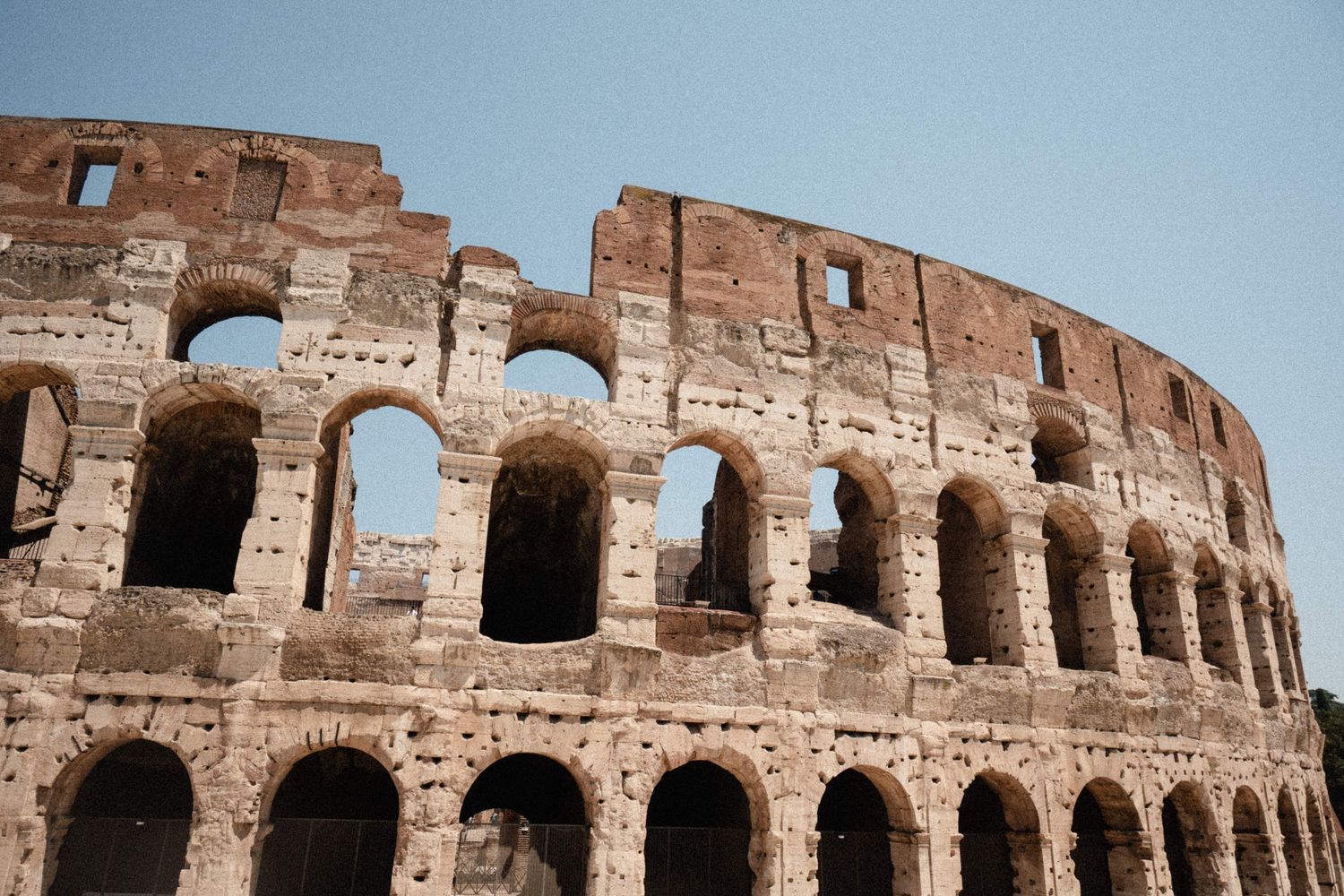 Ancient Roman Colosseum exterior showcasing iconic arched architecture against a clear blue sky in Rome, Italy.