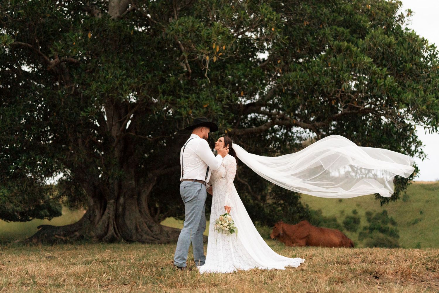 A blonde woman sits on a wooden floor holding a camera, wearing jeans and a white tank top against a dark backdrop.