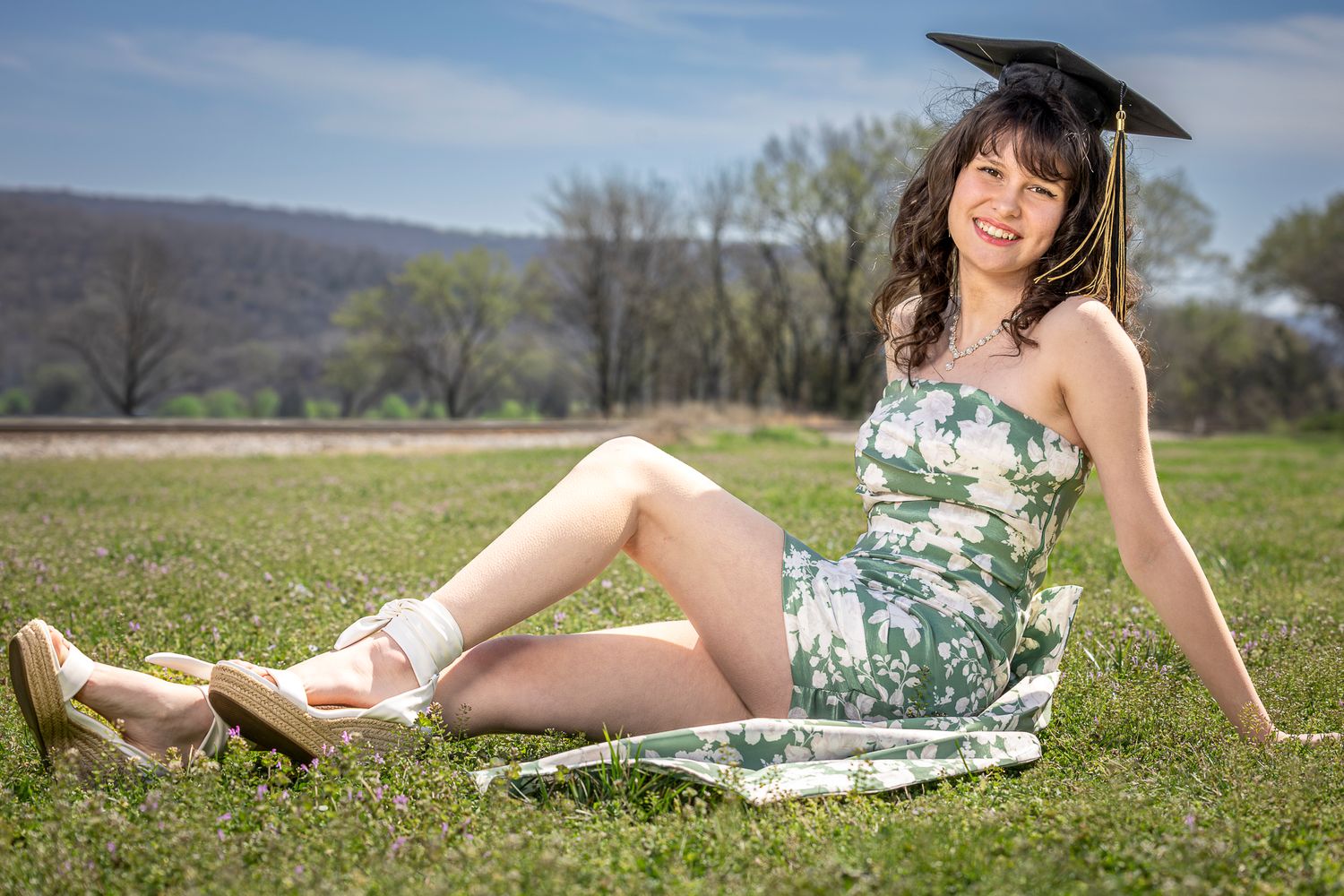 A person relaxes on a blanket in a green spring meadow with mountains visible in the background.