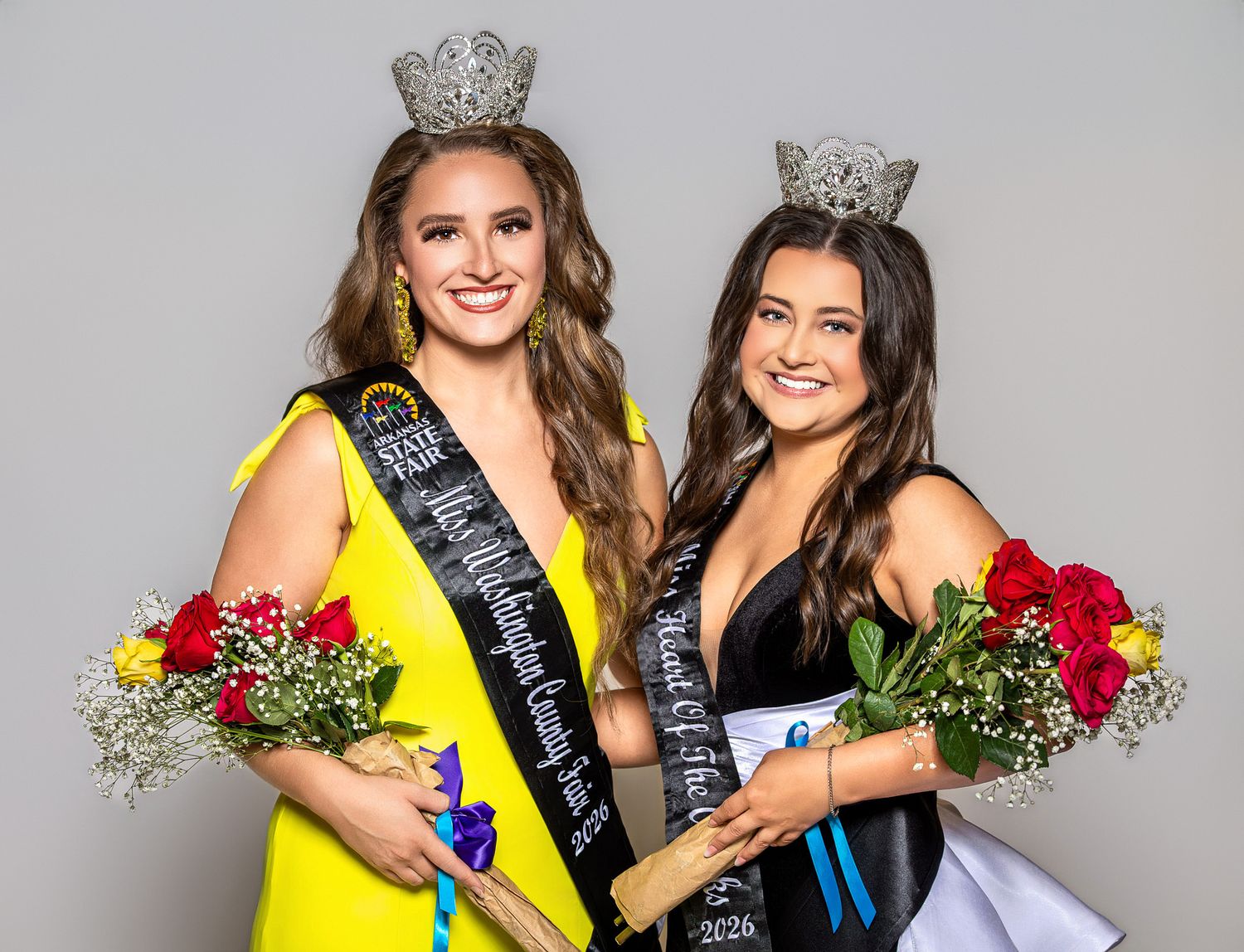 Three beauty queens in formal gowns and crowns pose together wearing pageant sashes at a competition.