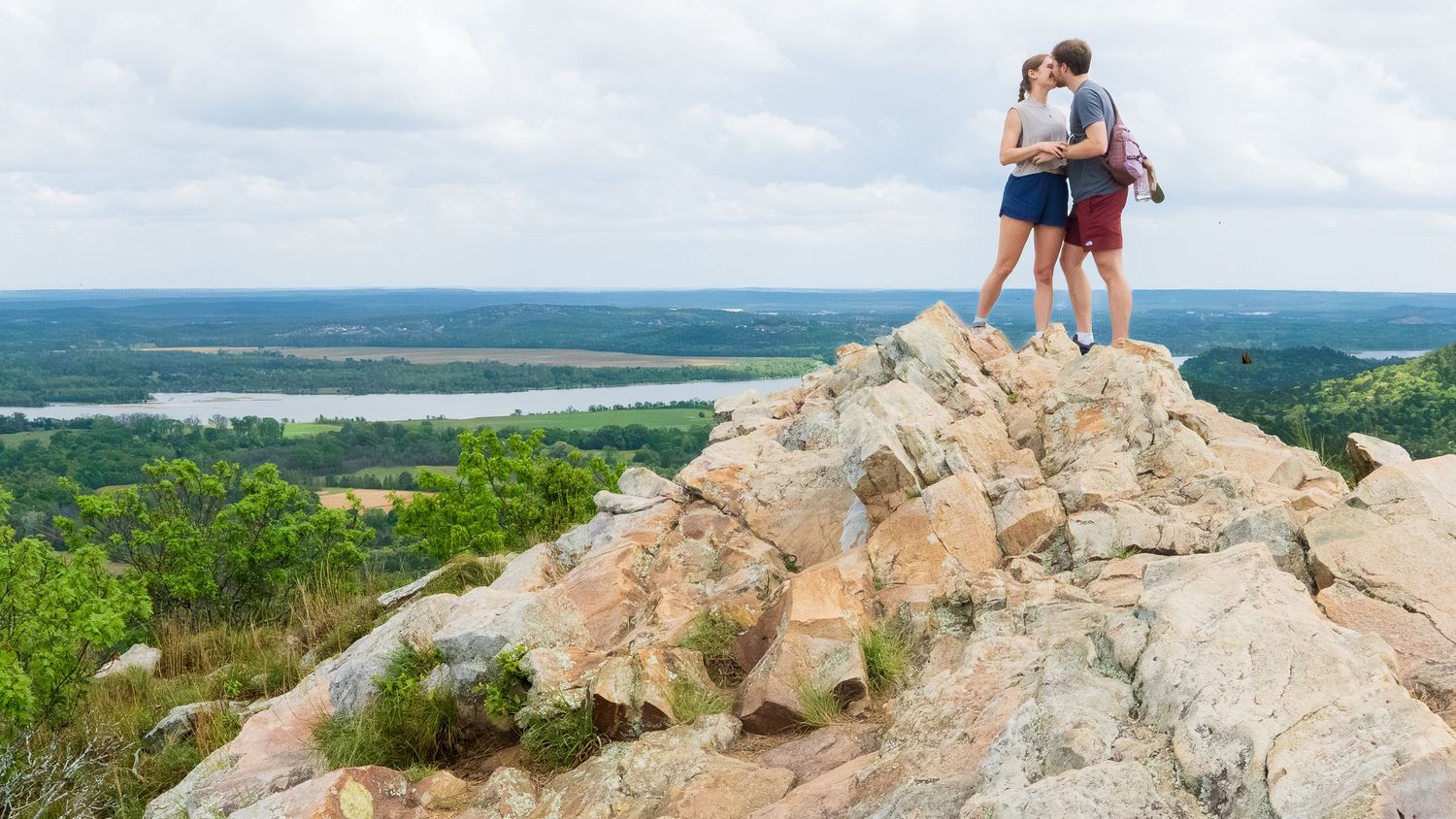 Young couple kisses at the peak of a rocky mountain top with a river view down below. Pinnacle Mountain in Little Rock, Arkansas