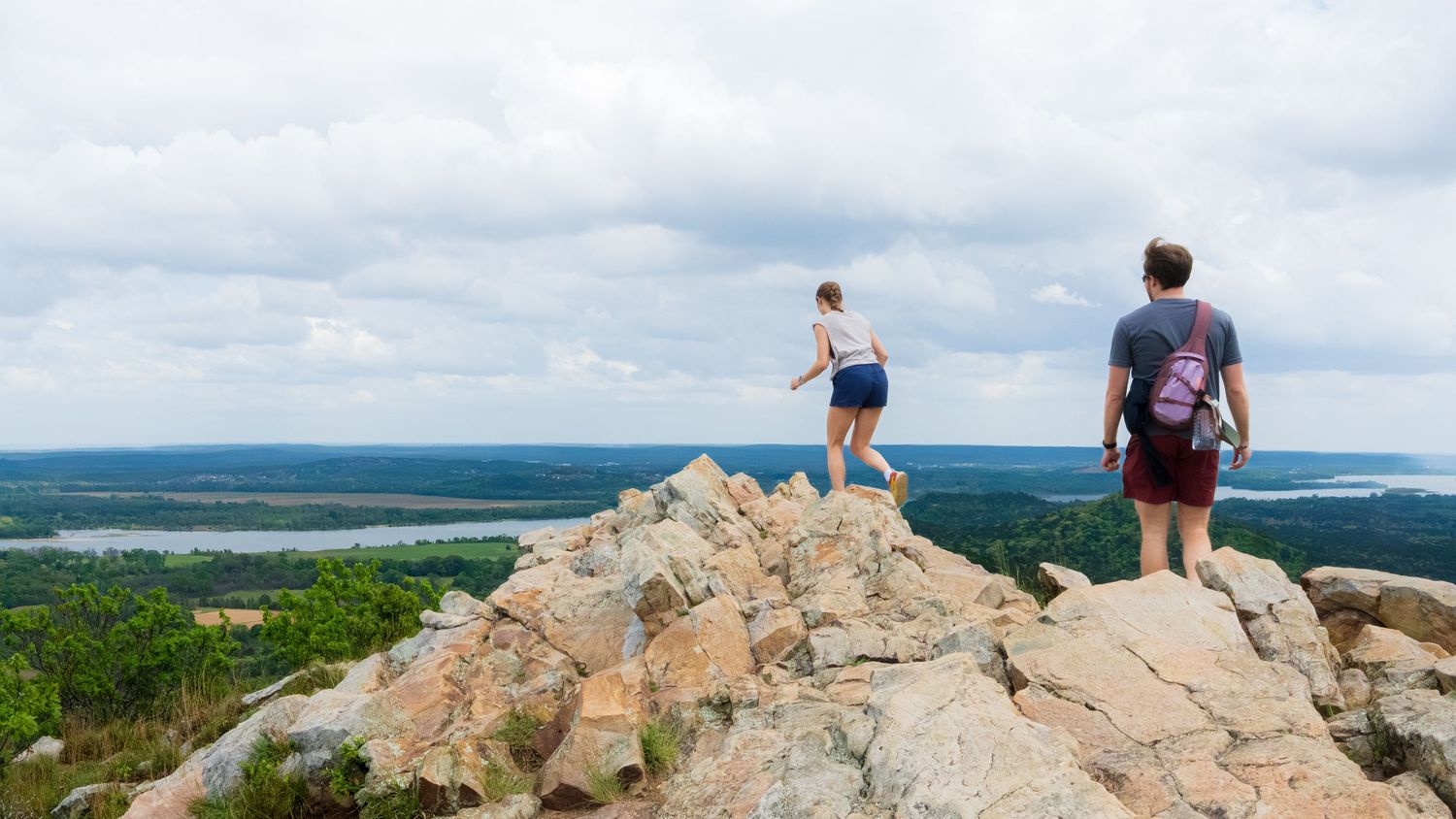 Young couple walks away along a rocky mountain top with a river view down below. Pinnacle Mountain in Little Rock, Arkansas