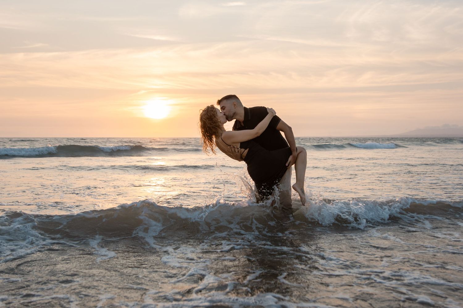 A silhouetted figure splashes through ocean waves at sunset creating a dramatic spray of water against an orange sky.
