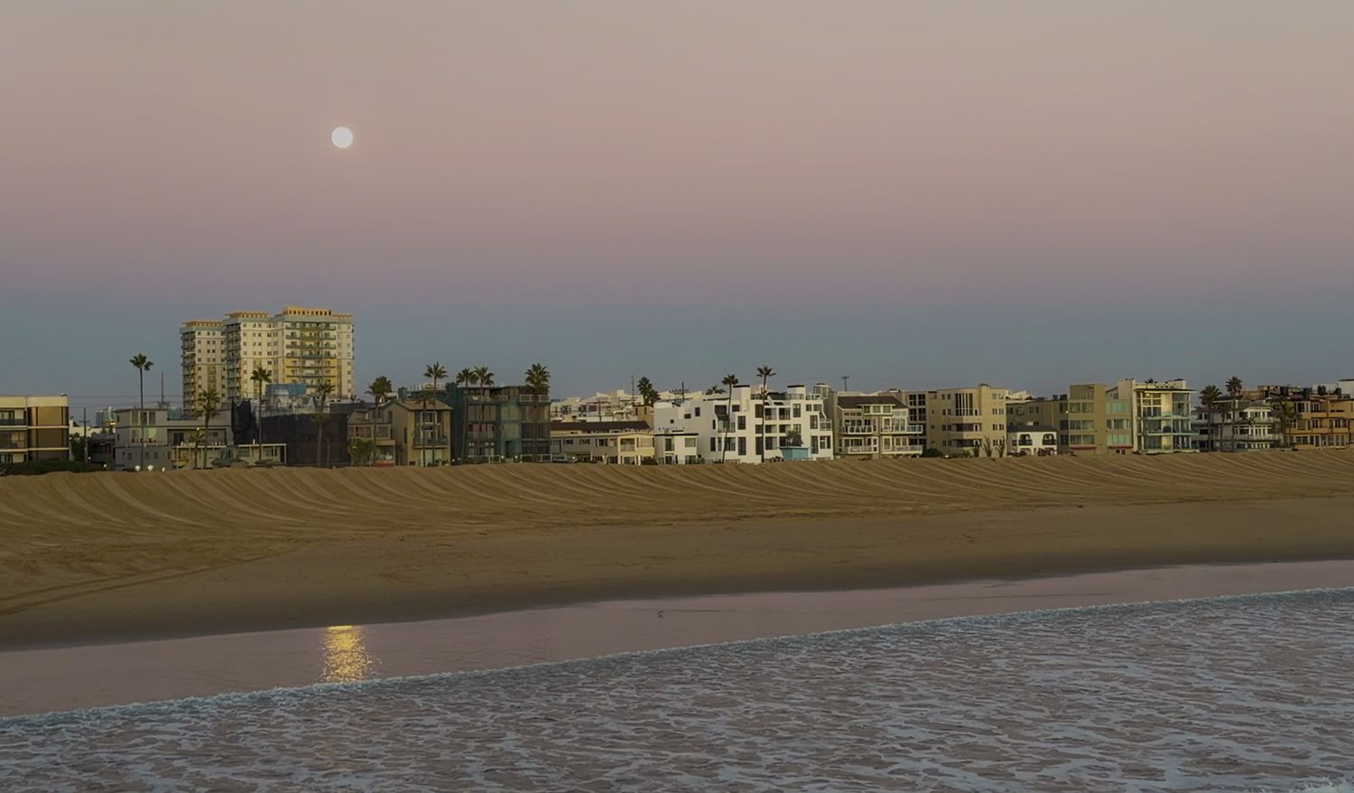 Panoramic sunset view of a beachfront cityscape with modern buildings and apartments along the shoreline.