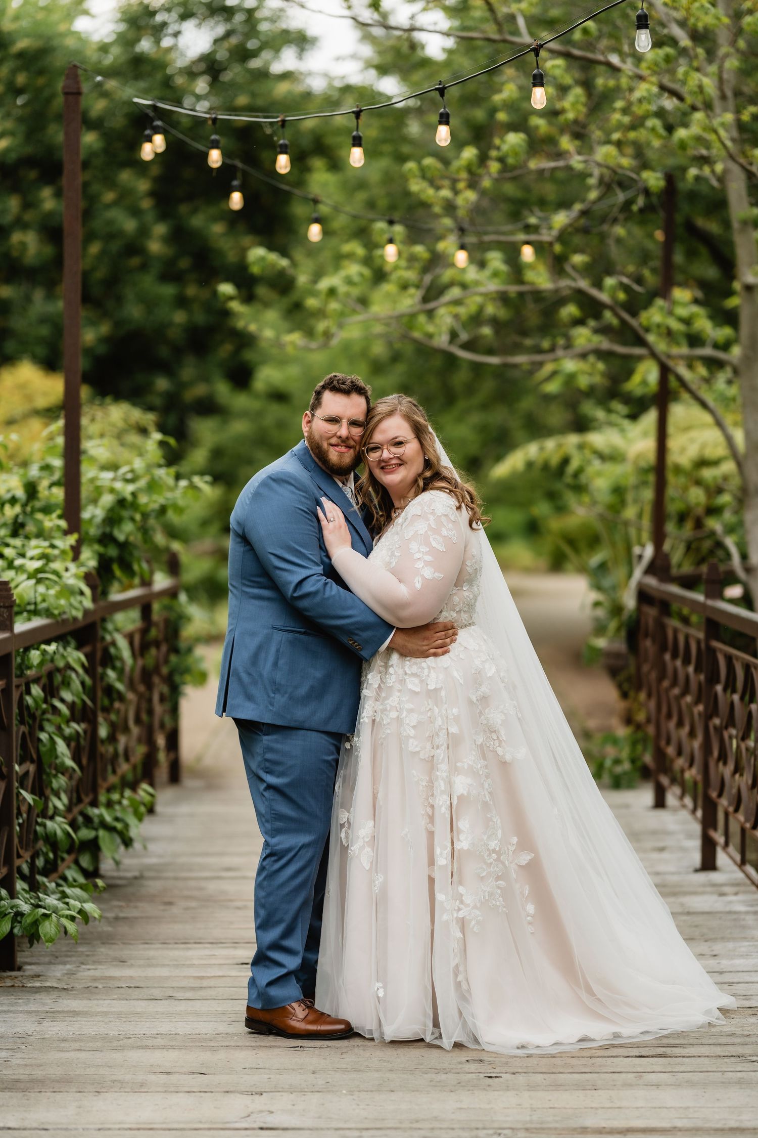 Tyler + Sarra embrace in their wedding outfits on a bridge.