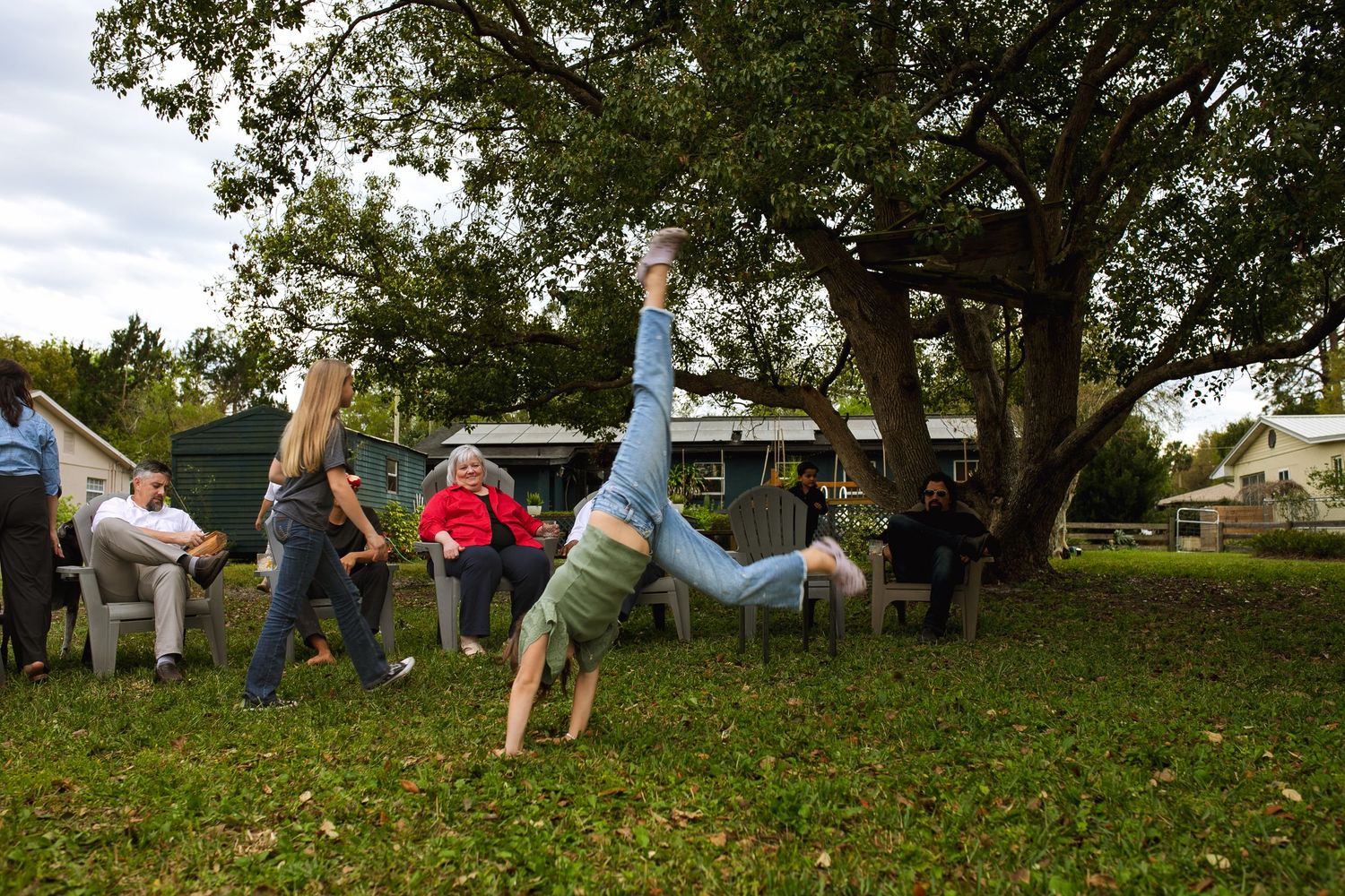 People having fun doing cartwheels and handstands on a grassy lawn with trees and parked cars in the background.