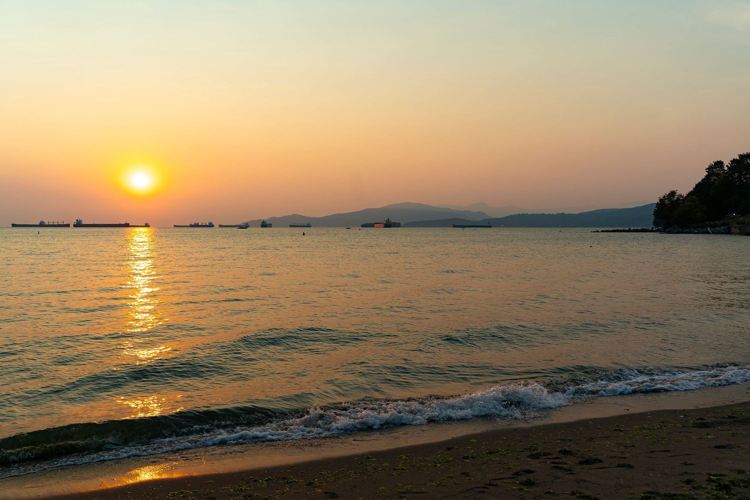 Panorama-Aufnahme eines Sonnenuntergangs über ruhigem Meer mit Booten vor einem leuchtend orangefarbenen Himmel.