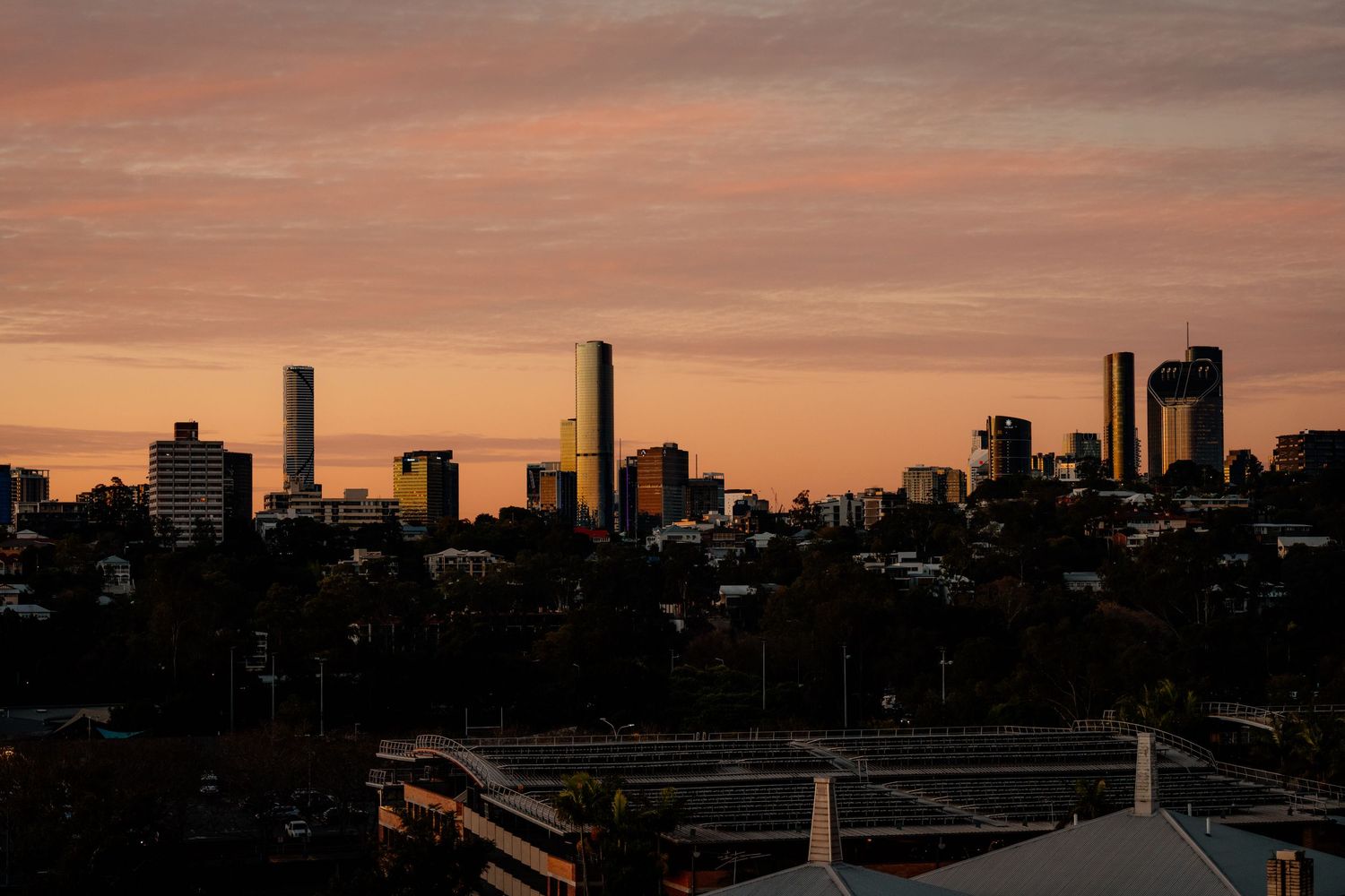 Panoramic cityscape silhouette at sunset with orange sky.