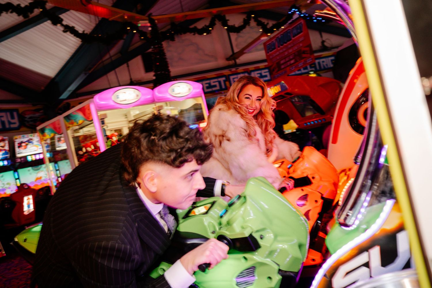 Bride and groom playing together in Weymouth arcade during their New Year’s Eve wedding on kids motorbike game