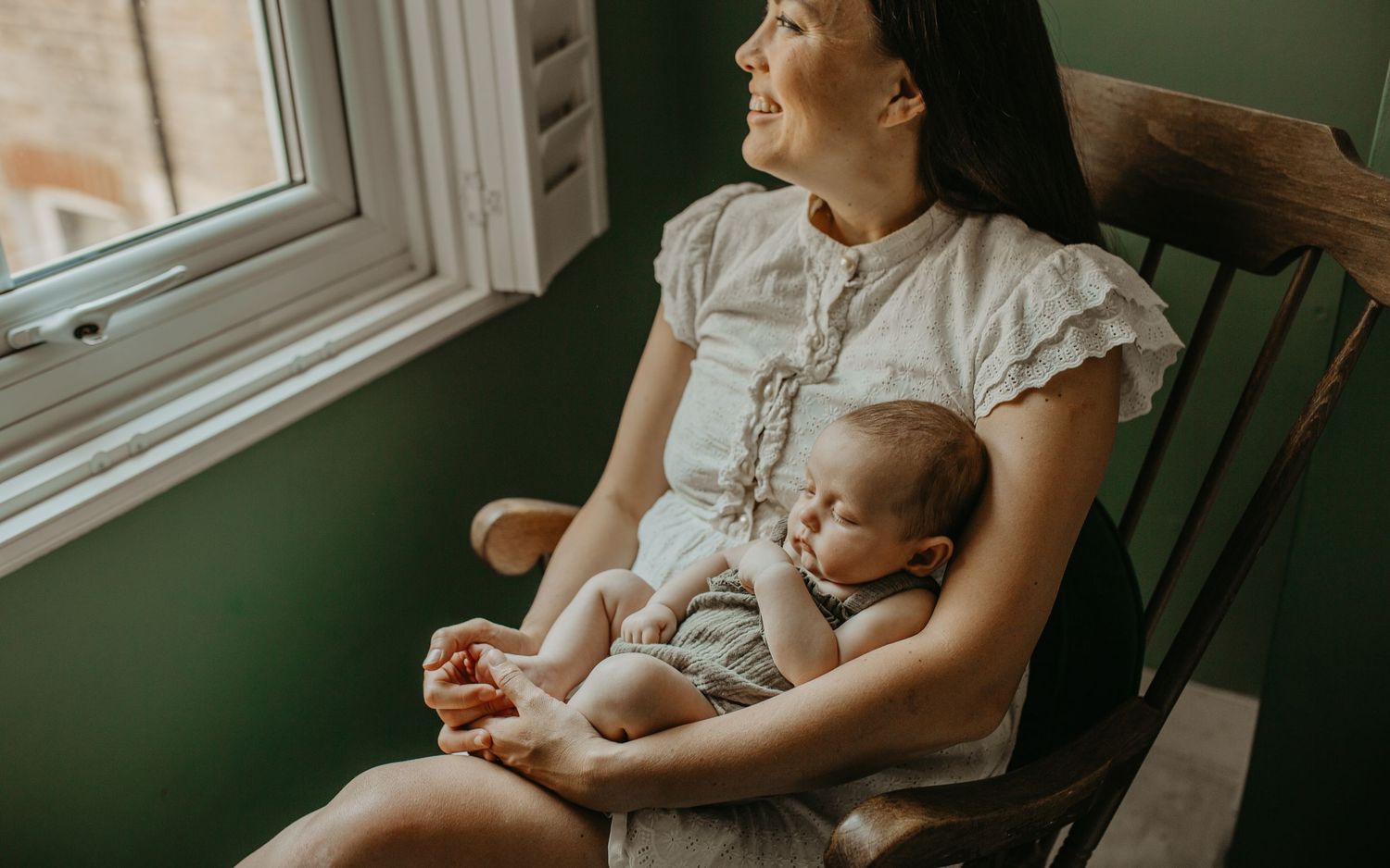 A tender moment between parent and infant in soft window light as they sit together in a rocking chair.