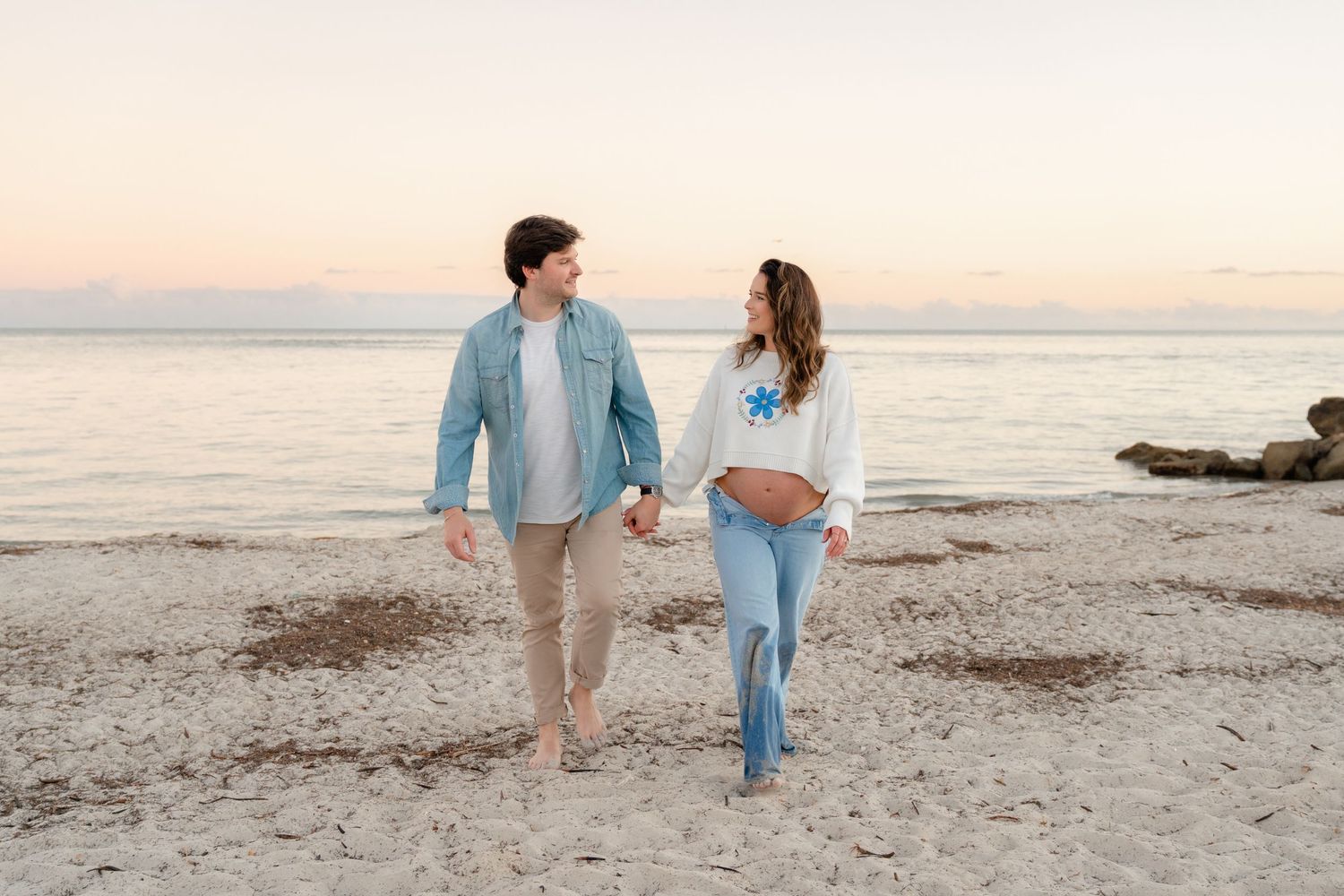 Couple walking together on a sandy beach at sunset wearing coordinated blue and white outfits.