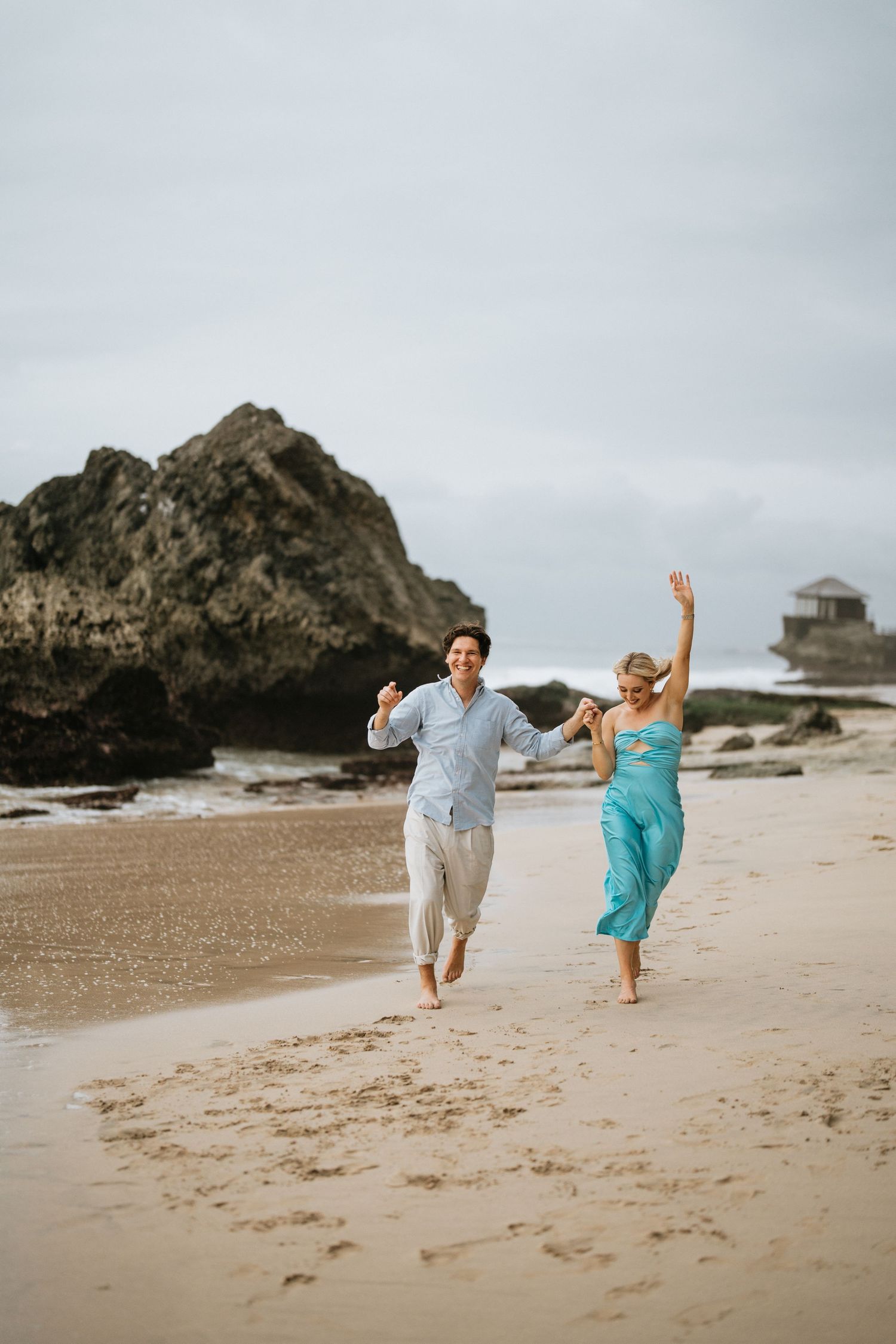 A couple embraces on a rocky beach landscape during cloudy weather.