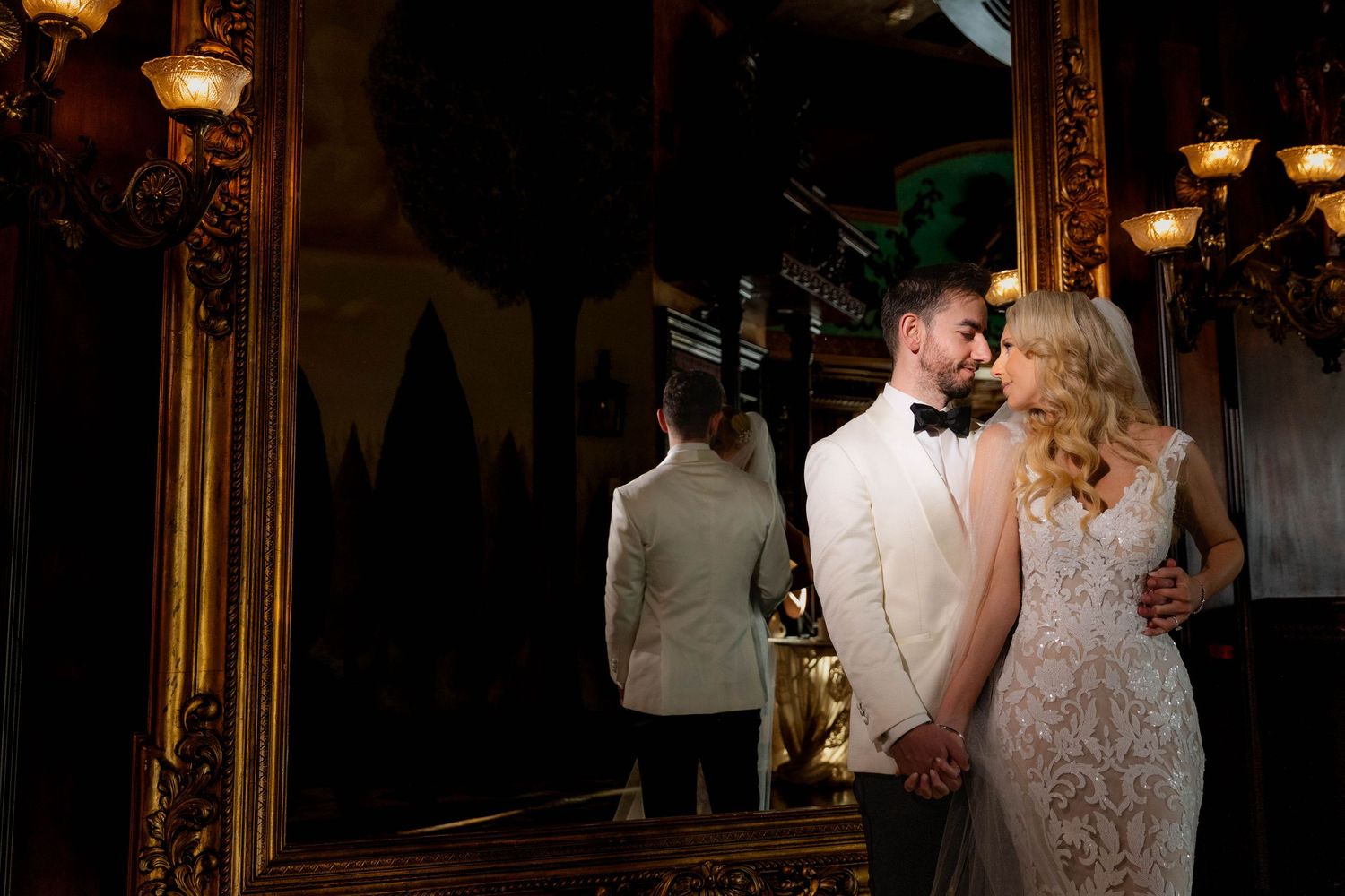 A bride and groom share romantic moments in a lush garden setting with elegant white columns and greenery.