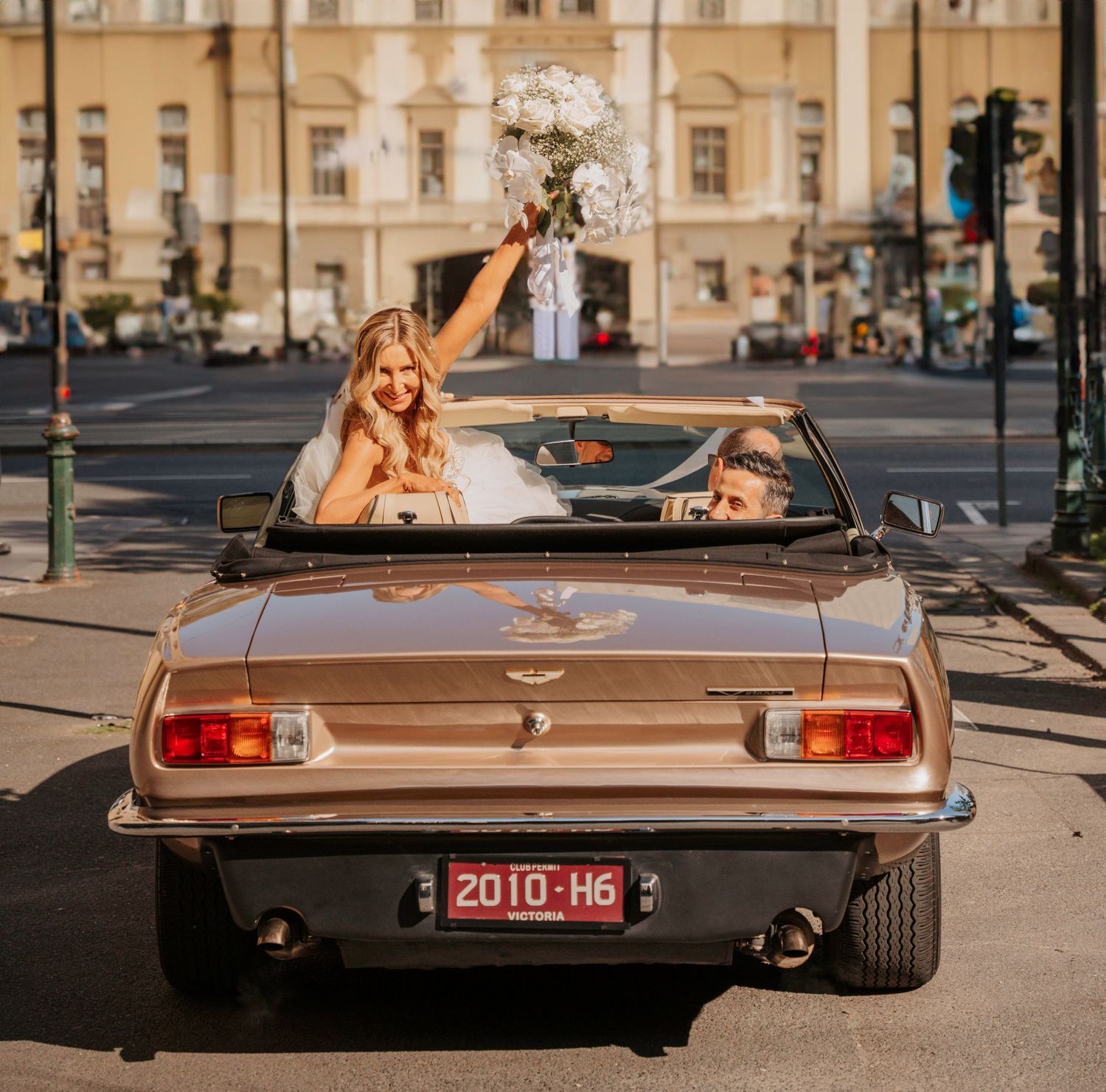 Classic vintage convertible car with brown metallic paint parked on a city street during sunset.