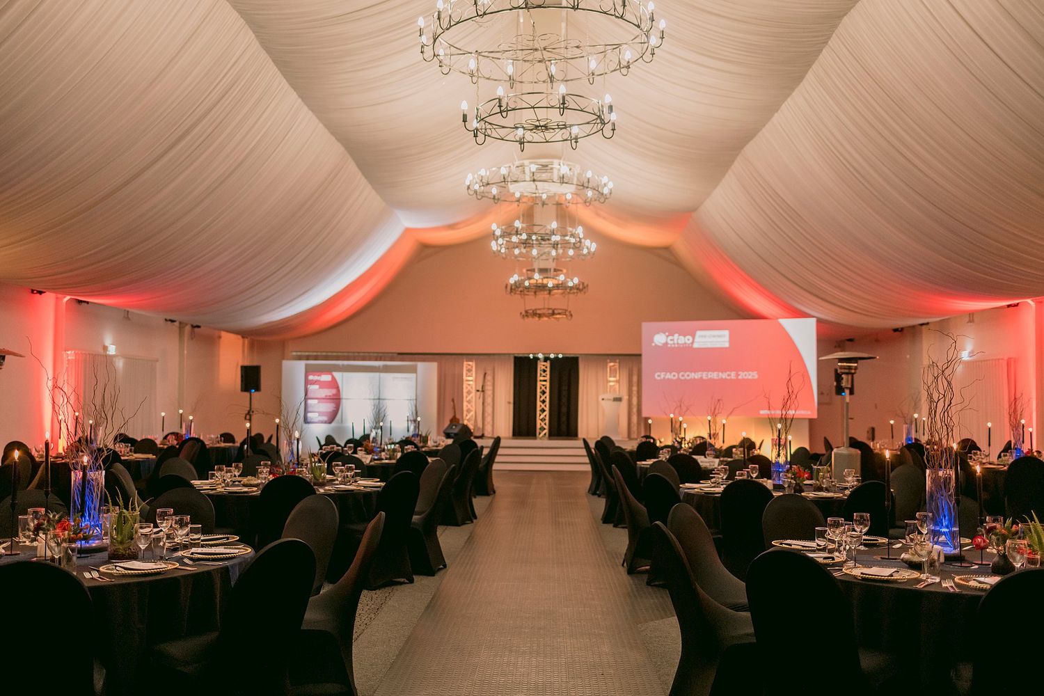 Elegant event venue with chandelier lighting, round tables, and red ambient lighting.