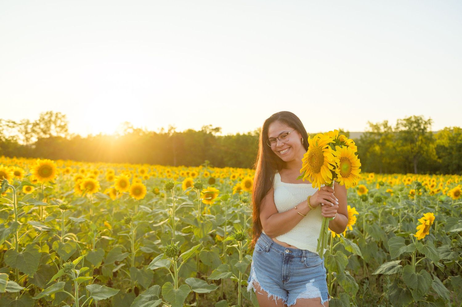 Woman in blue dress standing in a vibrant sunflower field during golden hour sunset.