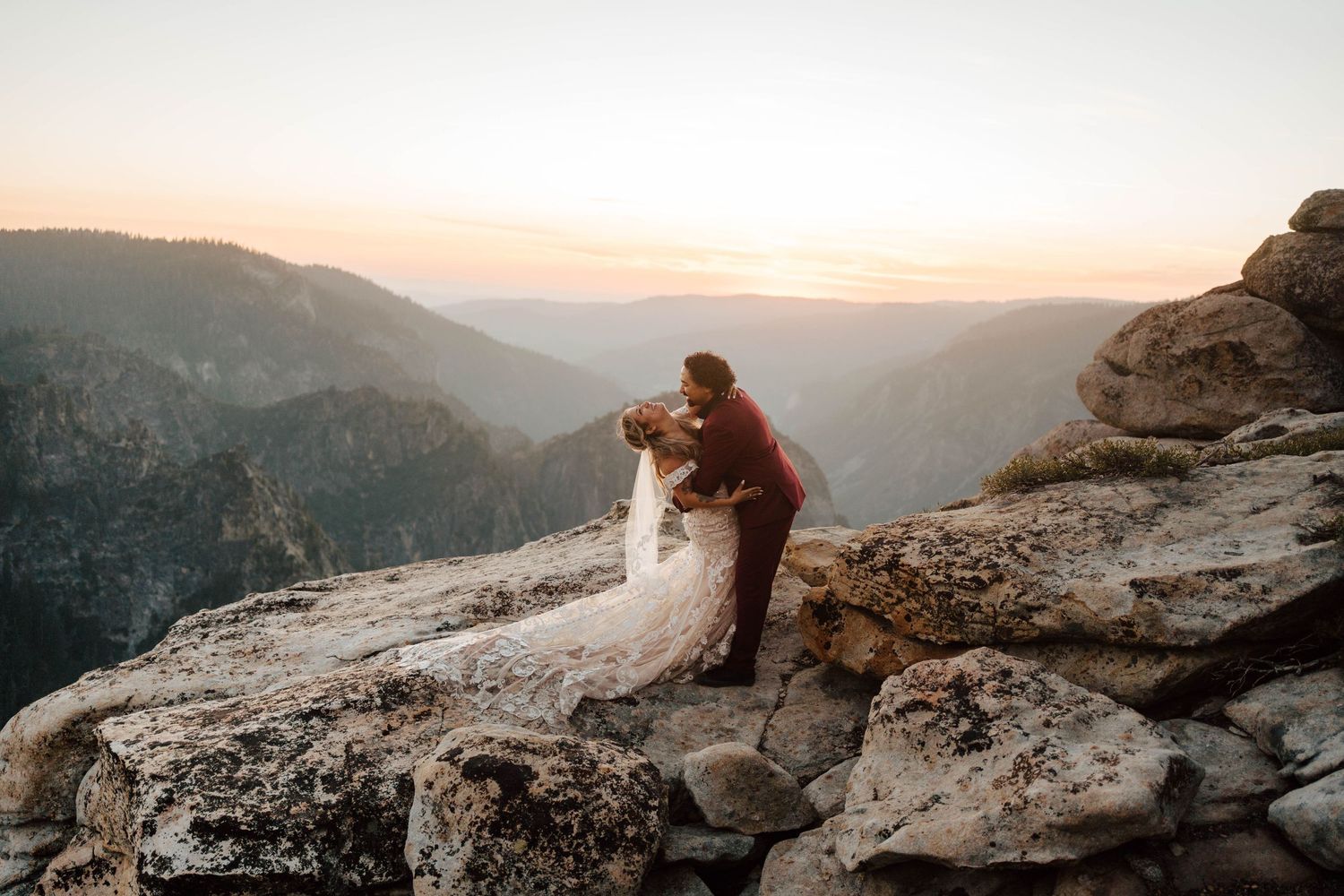 Couple shares romantic dip kiss on rocky Yosemite cliff at golden hour sunset.