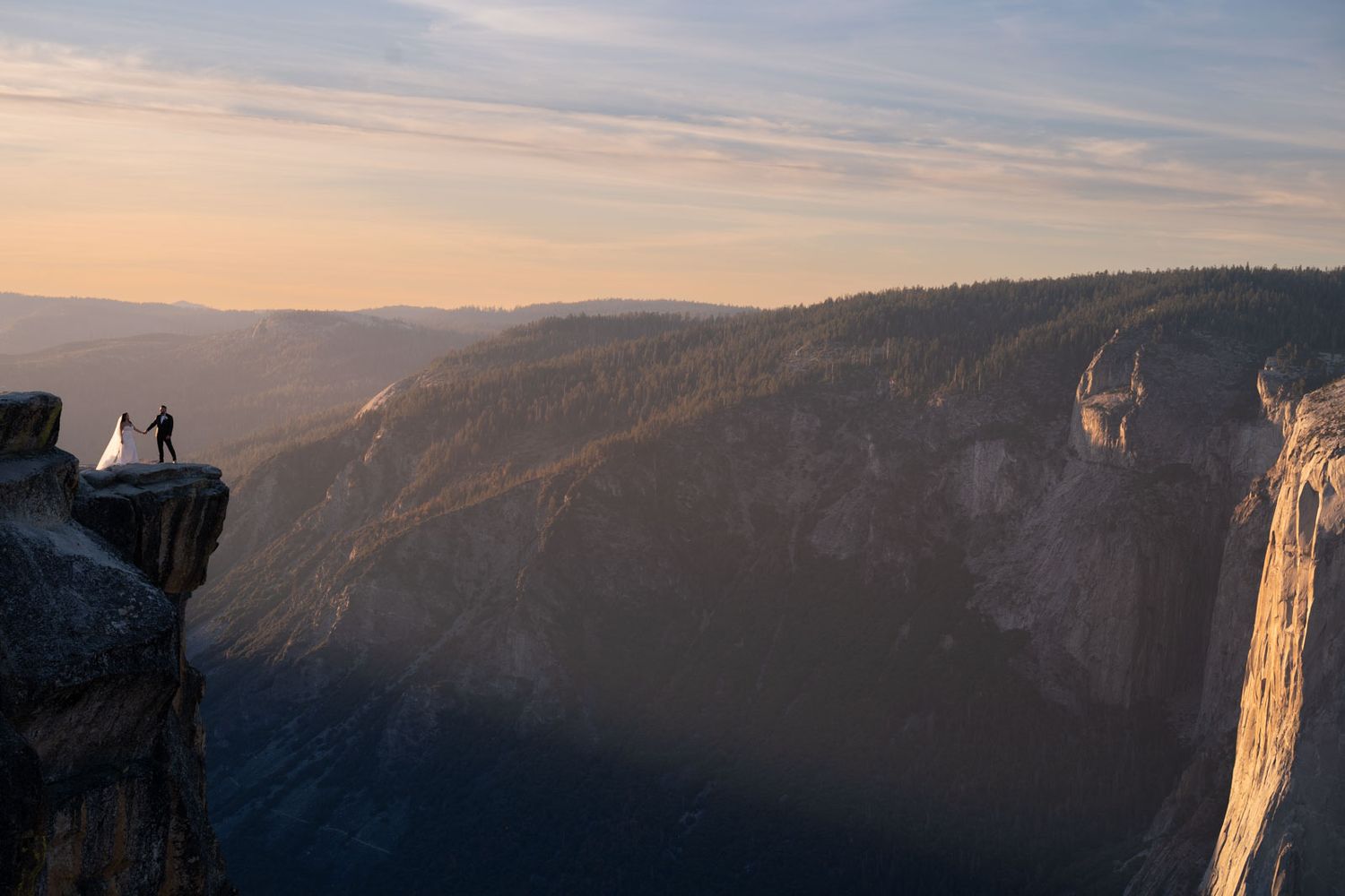 A panoramic view at taft point at sunset with an elopement couple standing on a cliff against a dramatic orange and blue sky.