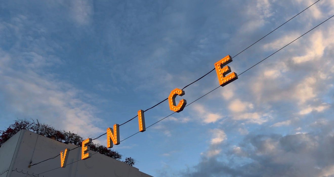 A panoramic view of a cloudy blue sky with orange letters spelling out VENICE mounted on a building rooftop.