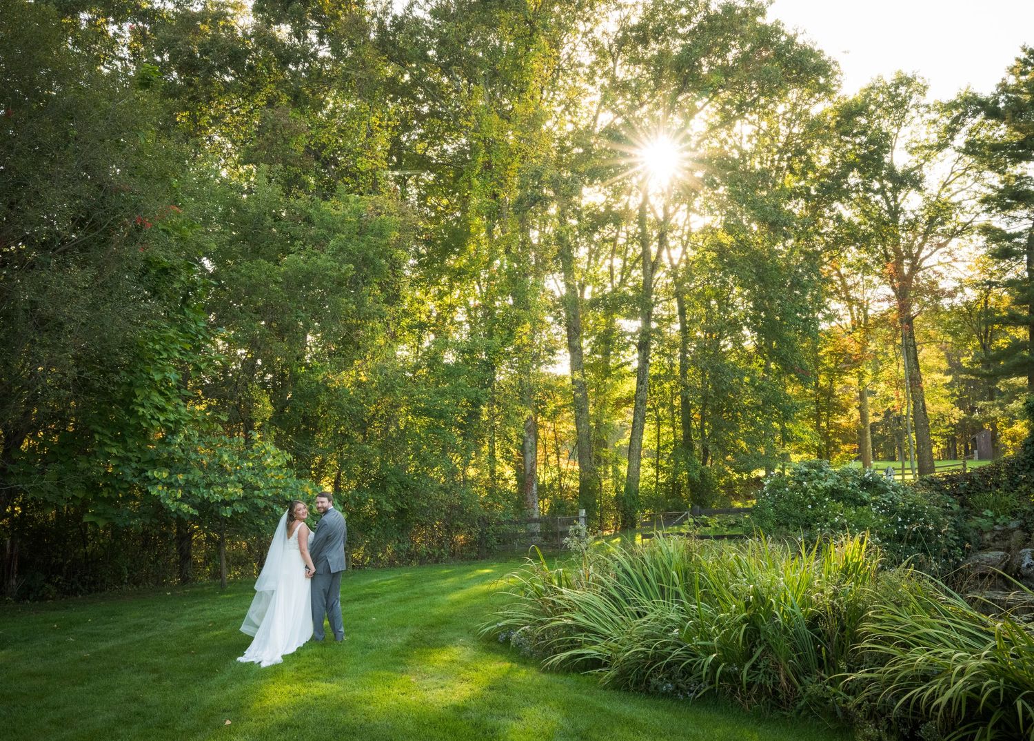 Newlyweds share an intimate moment outdoors with autumn foliage and rustic architecture in background.