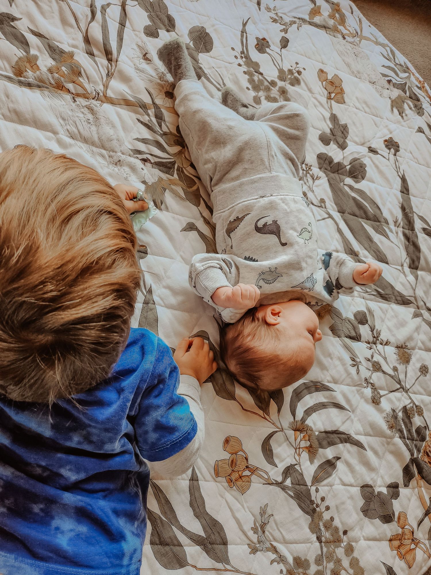Two children resting on floral patterned bedding wearing blue clothing.