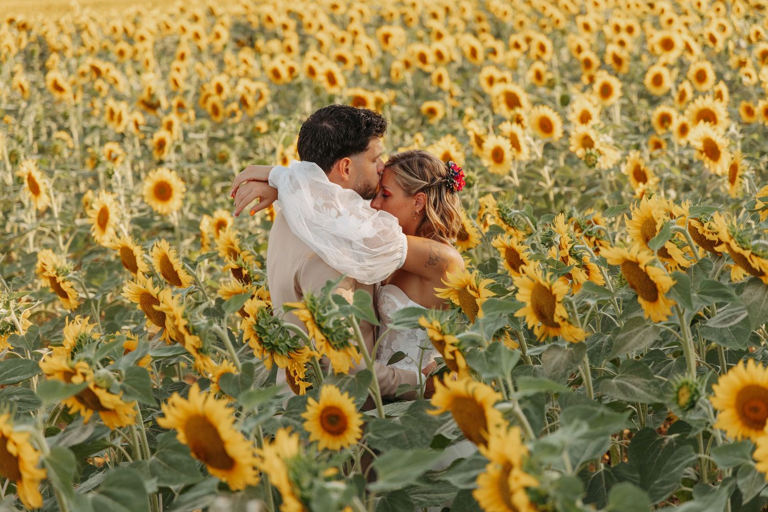 Couple embracing and lifting each other joyfully surrounded by tall blooming sunflowers in a field.