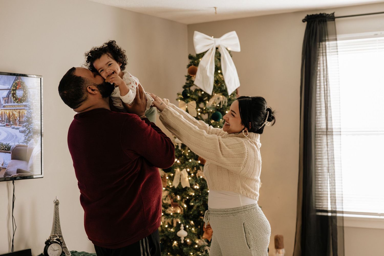 A couple dances together in front of a decorated Christmas tree in their living room.
